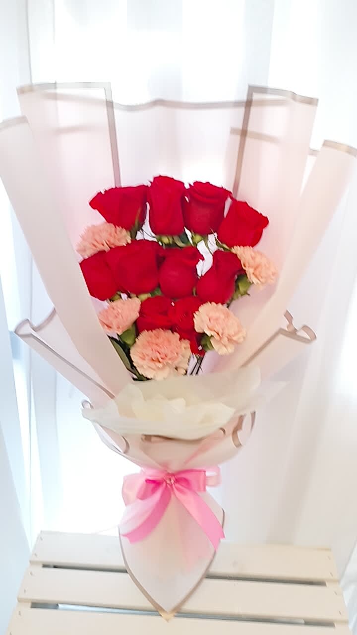 Bouquet of red roses and pale pink carnations wrapped in blush paper