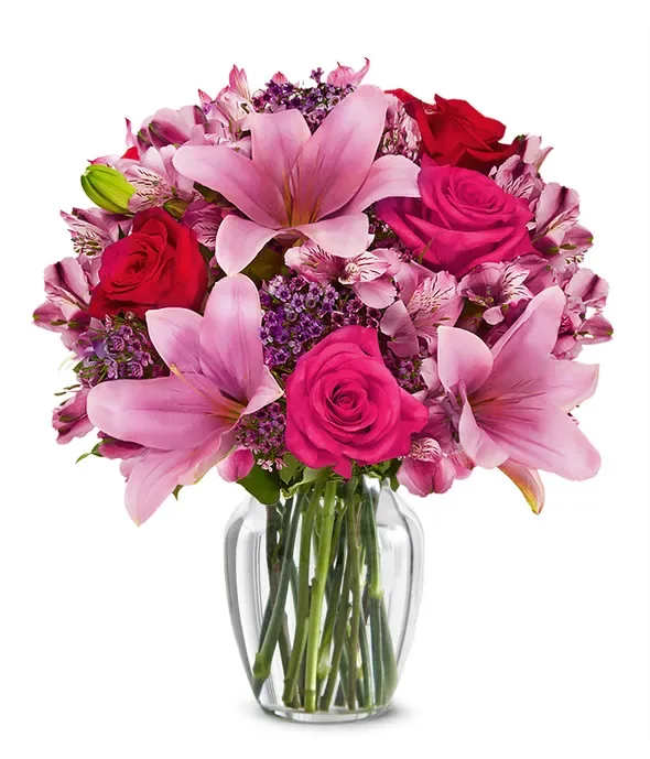 Pink lilies and roses arranged in a clear glass vase