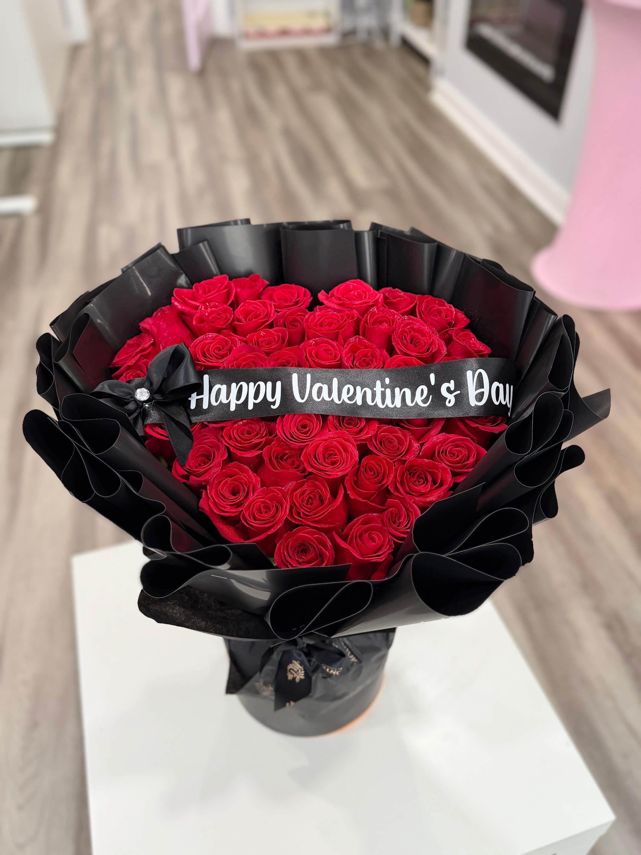 Bouquet of red roses wrapped in black paper with a Valentine’s Day ribbon