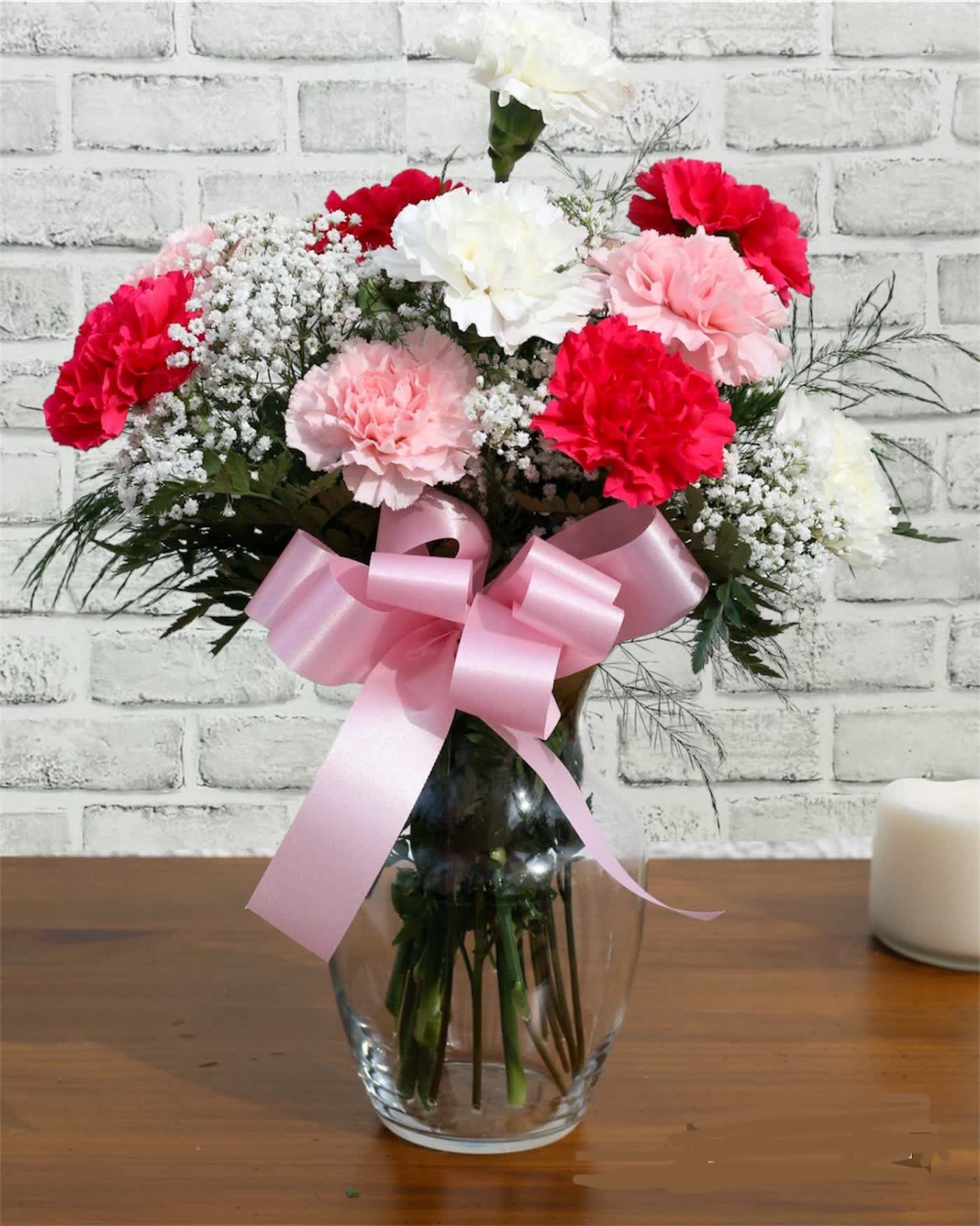 Pink and white carnations in a glass vase with a pink ribbon
