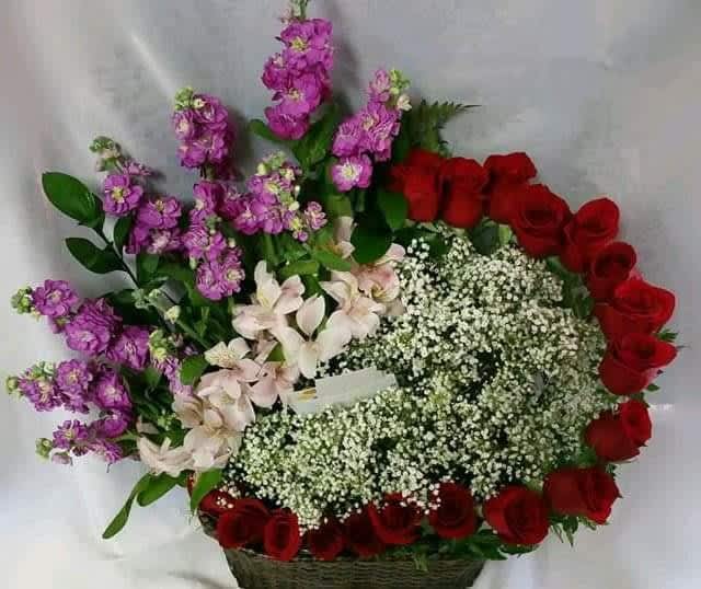 Basket arrangement of red roses, purple stock, and white baby's breath