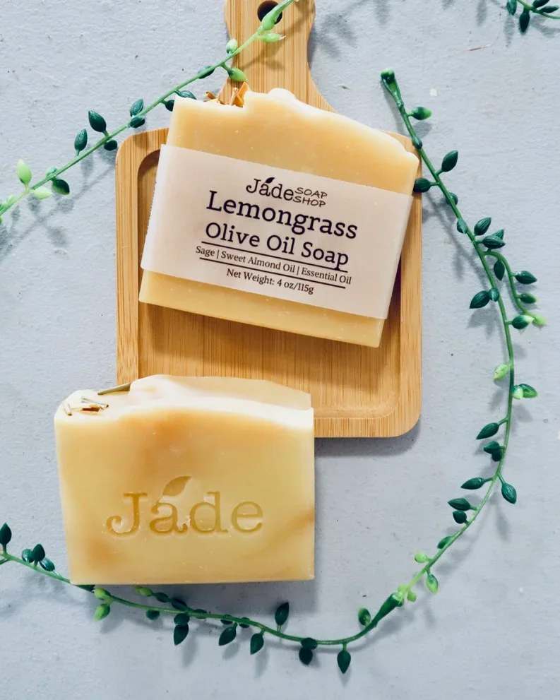 Two beige lemongrass olive oil soap bars on a wooden board with a trailing vine accent.