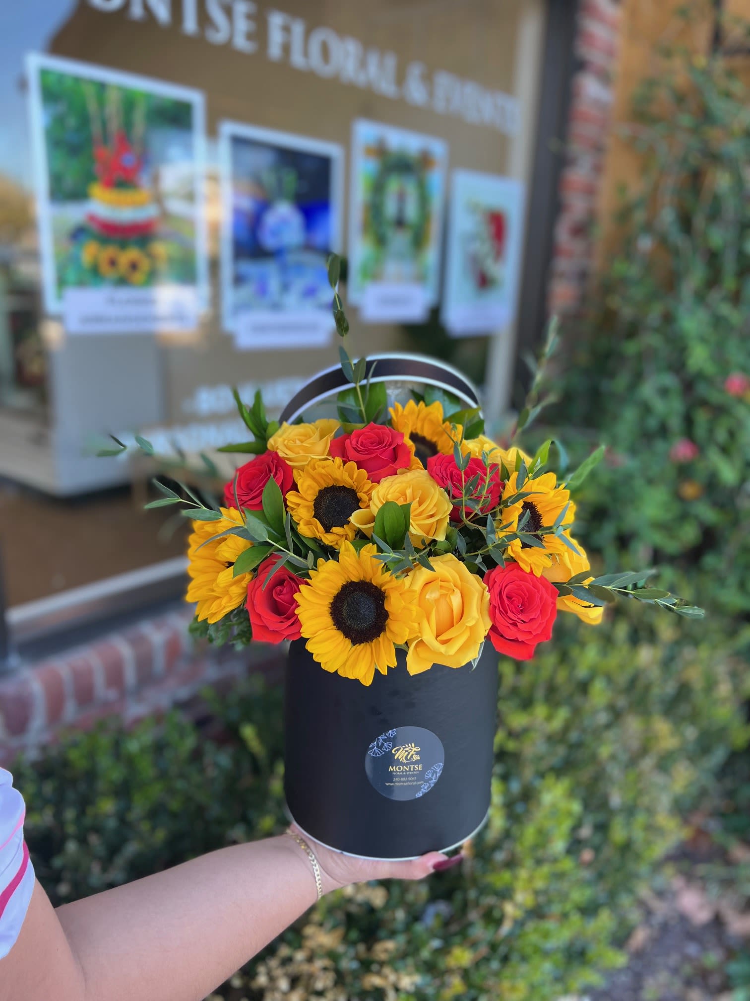 Bouquet of red and yellow roses with sunflowers in a black hat box