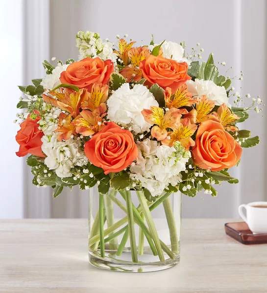 Orange roses and white flowers arranged in a clear glass vase