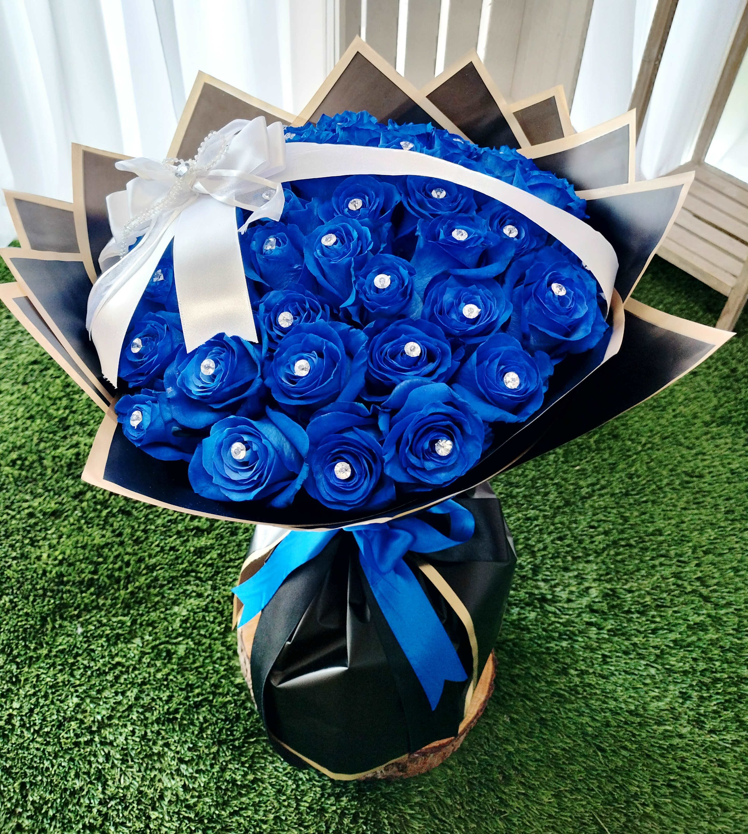 Bouquet of bright blue roses wrapped in black paper with a white ribbon