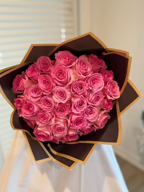 Bouquet of pink roses wrapped in dark paper with gold trim