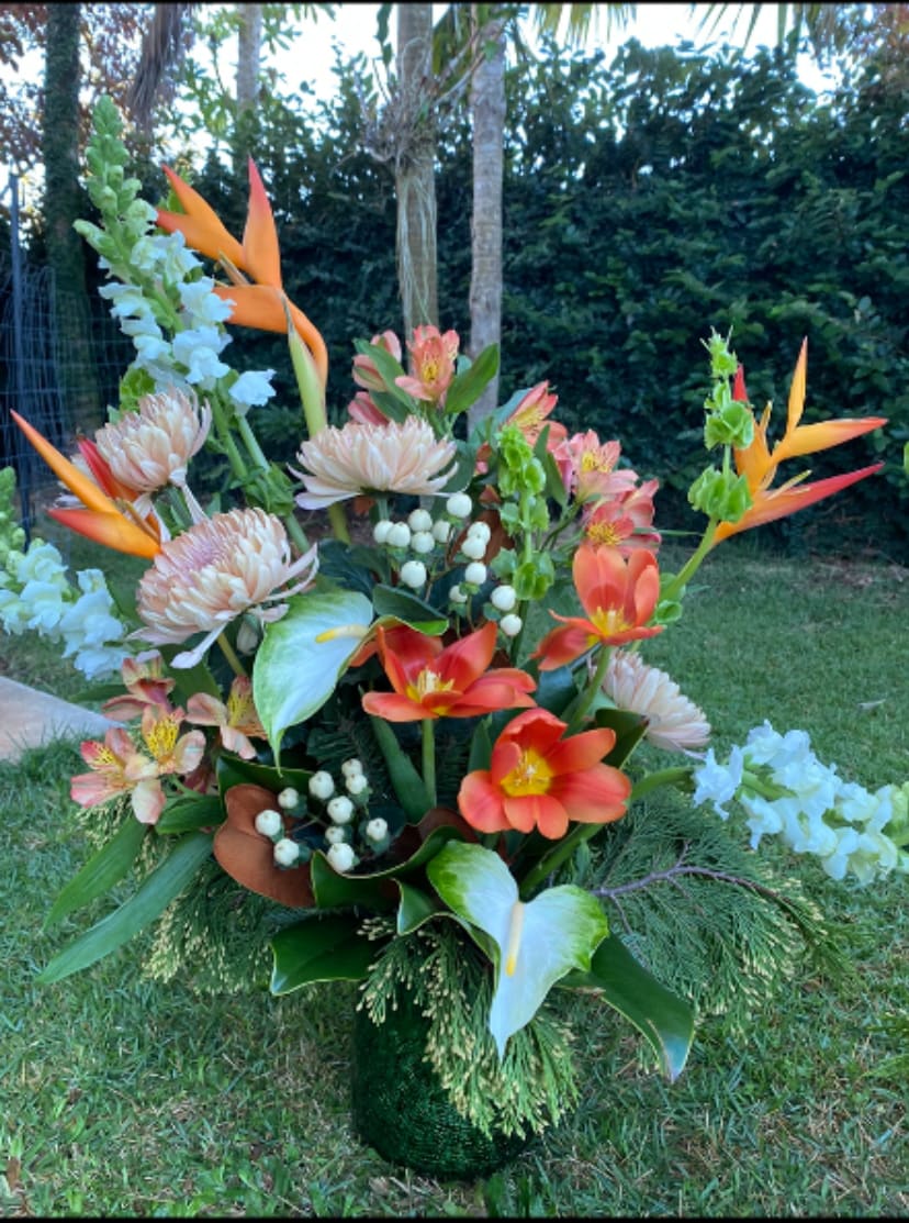 Tropical floral arrangement with orange birds of paradise and coral blooms in a green vase