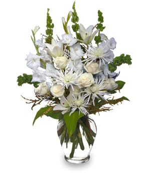 Tall arrangement of white lilies, roses, and mums with green accents in a clear glass vase