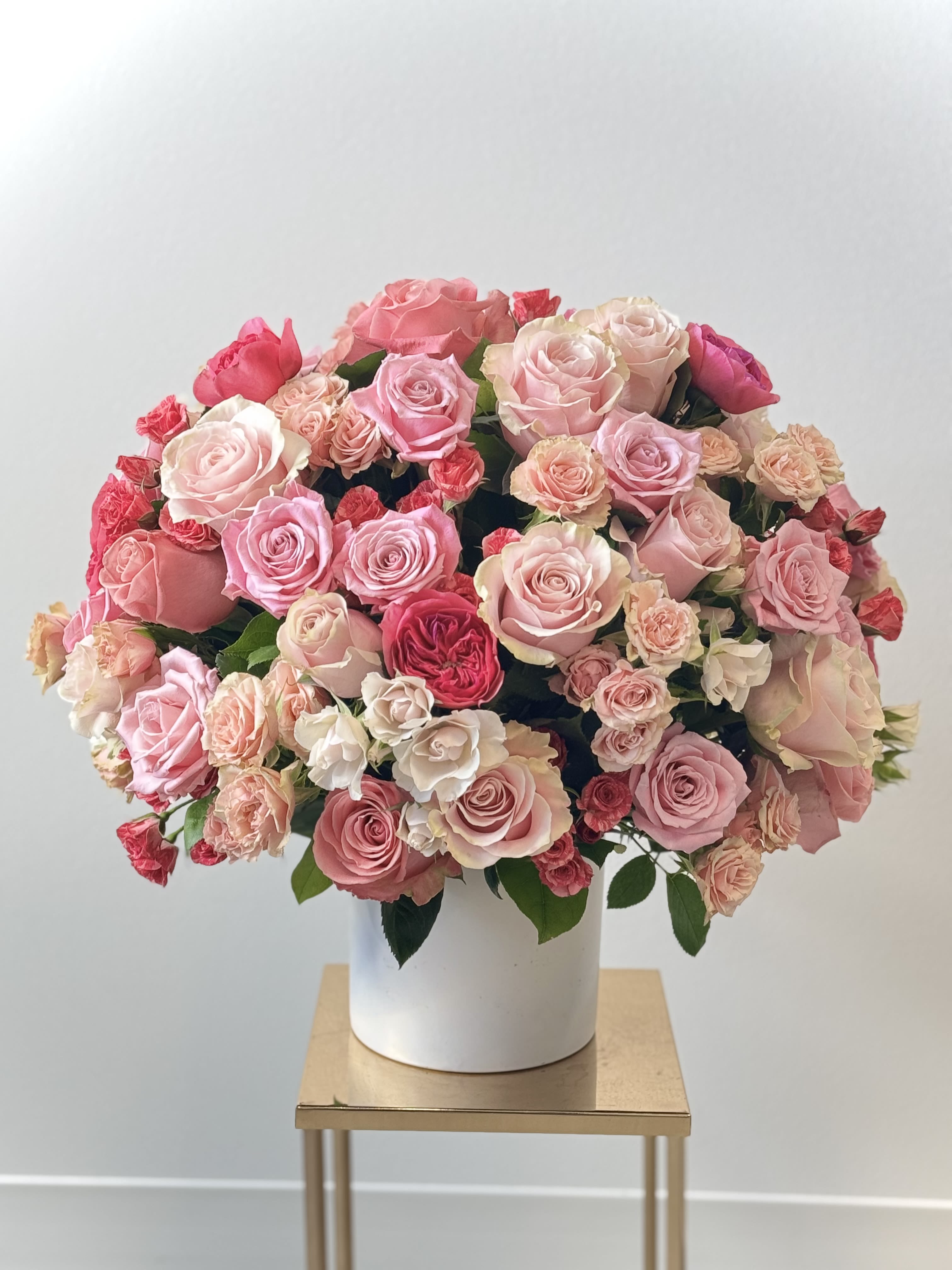 Lovely Romance - Behold a grand tribute to romance from Irvine Village Flowers! This resplendent bouquet, the pinnacle of rosy devotion, is a jubilant celebration crafted for those enchanted by the timeless rose. A lavish gathering of 70 premium garden roses, classic roses, and delicate spray roses unfurls in a symphony of blush and bloom, nestled within a stately round ceramic vase. For those who crave even greater splendor, the Deluxe edition boasts an opulent 100 roses, a veritable crown of floral majesty.  Premium will take her breath away with 120 roses.  Each rose, a petal-clad emissary of love, whispers tales of passion, adoration, and eternal promise. The garden roses reign with lush, velvety grandeur, while the spray roses sprinkle dainty bursts of charm, creating a bouquet that radiates both magnificence and tenderness. This is the ultimate gift, a rosy reverie to sweep your beloved into a world of heartfelt enchantment.  Spanning 18x18 inches in its Standard glory, 22x22 in Deluxe and an expansive 25x25 inches in Premium splendor, this all-around arrangement dazzles from every vantage point. Visit Irvine Village Flowers online or in-store to bestow this blooming treasure, and let our impeccable delivery ensure it arrives in full, fragrant splendor—a grand gesture for the rose-adoring soul!
