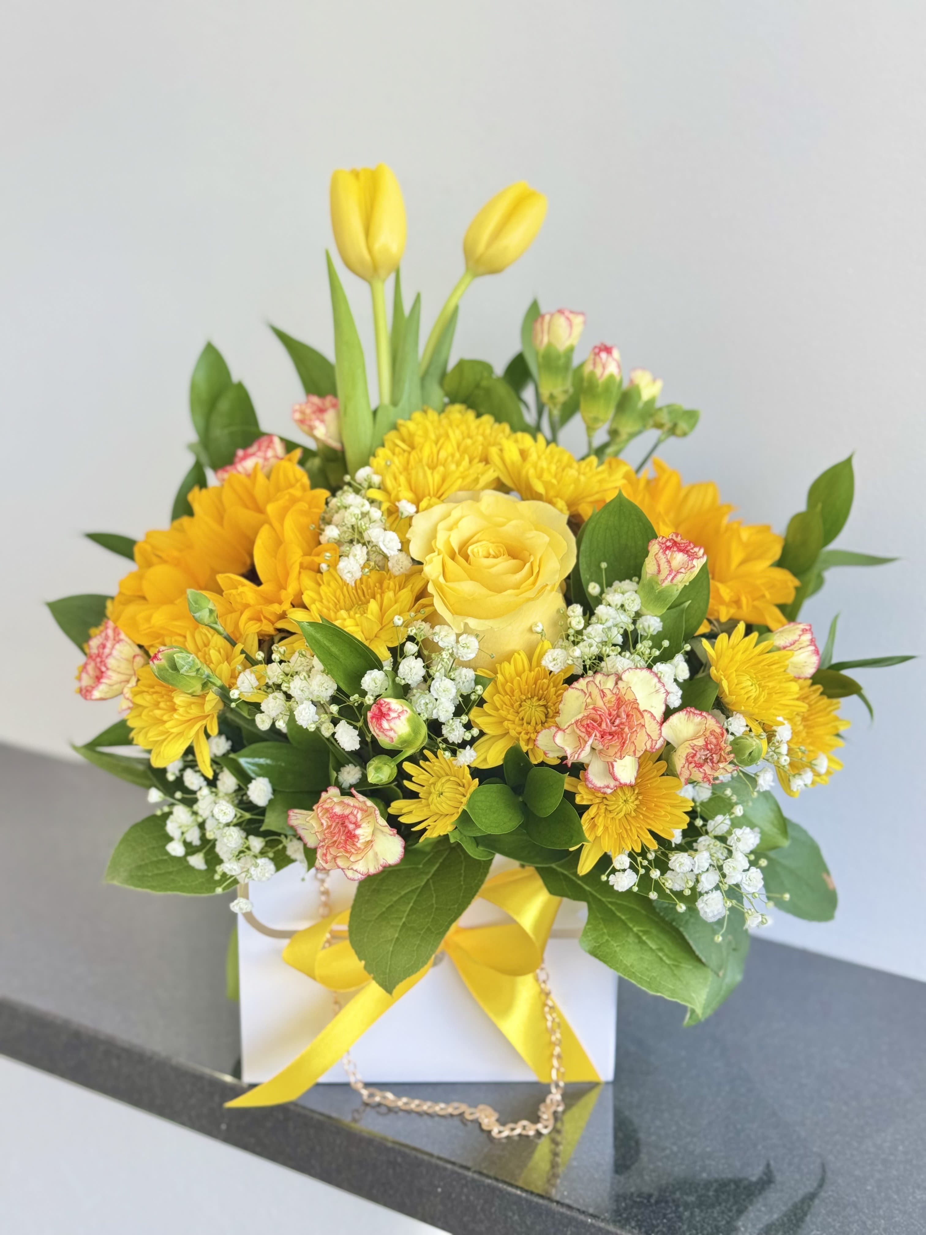 Yellow tulips and roses in a white gift box with a yellow ribbon