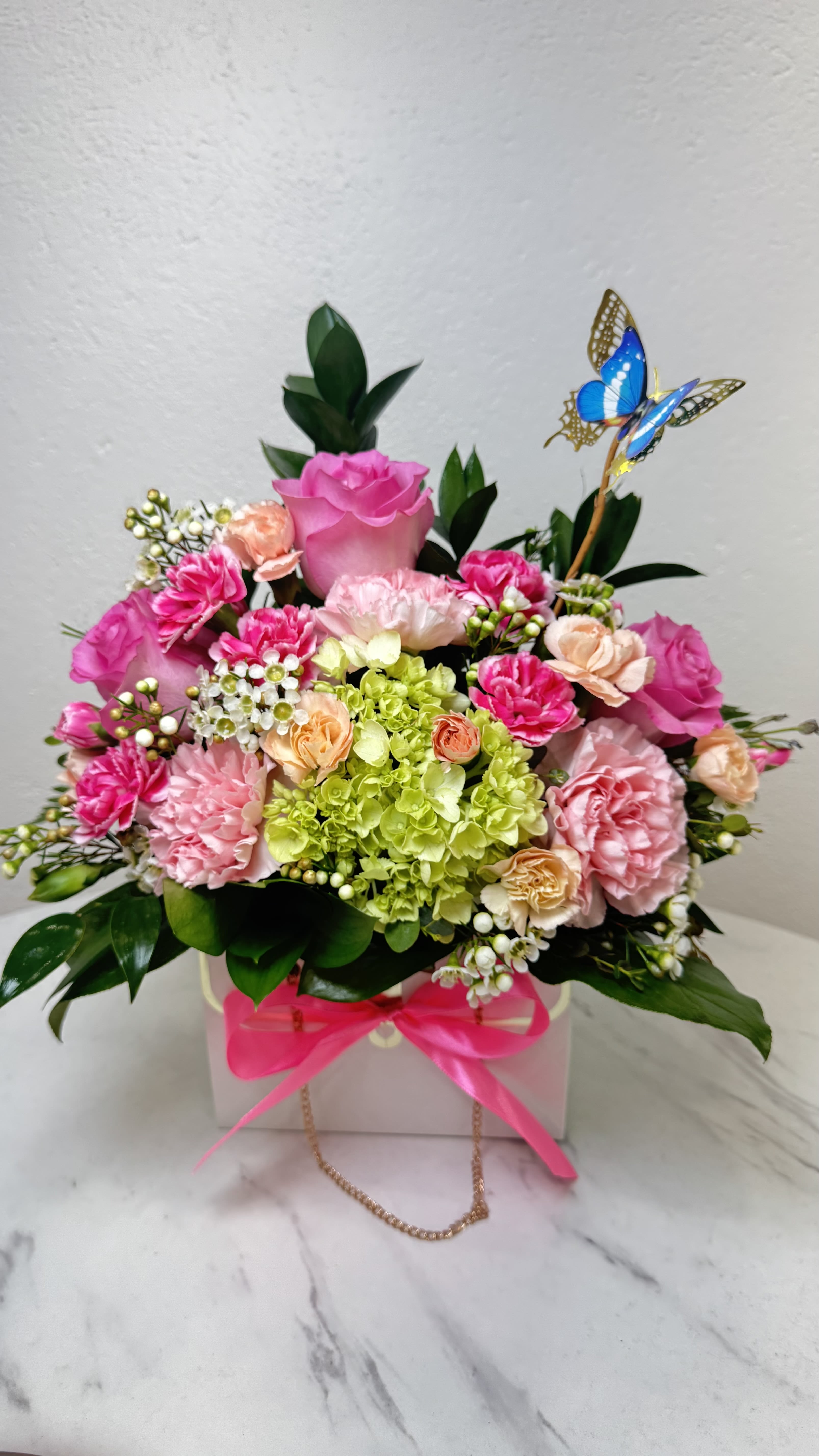 Pink and peach floral arrangement in a white box with a butterfly pick