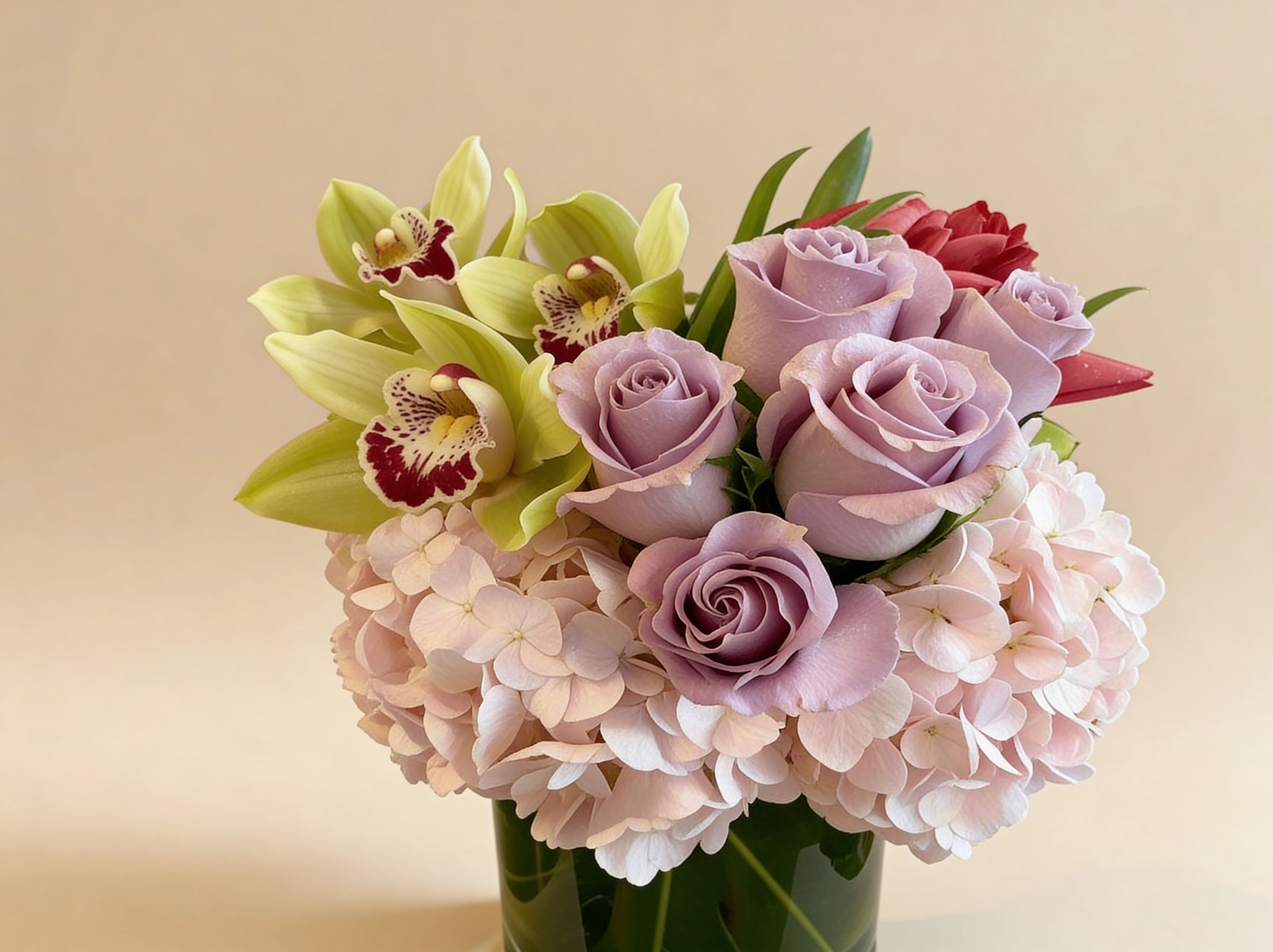 Low arrangement of lavender roses, green orchids, and blush hydrangeas in a glass vase