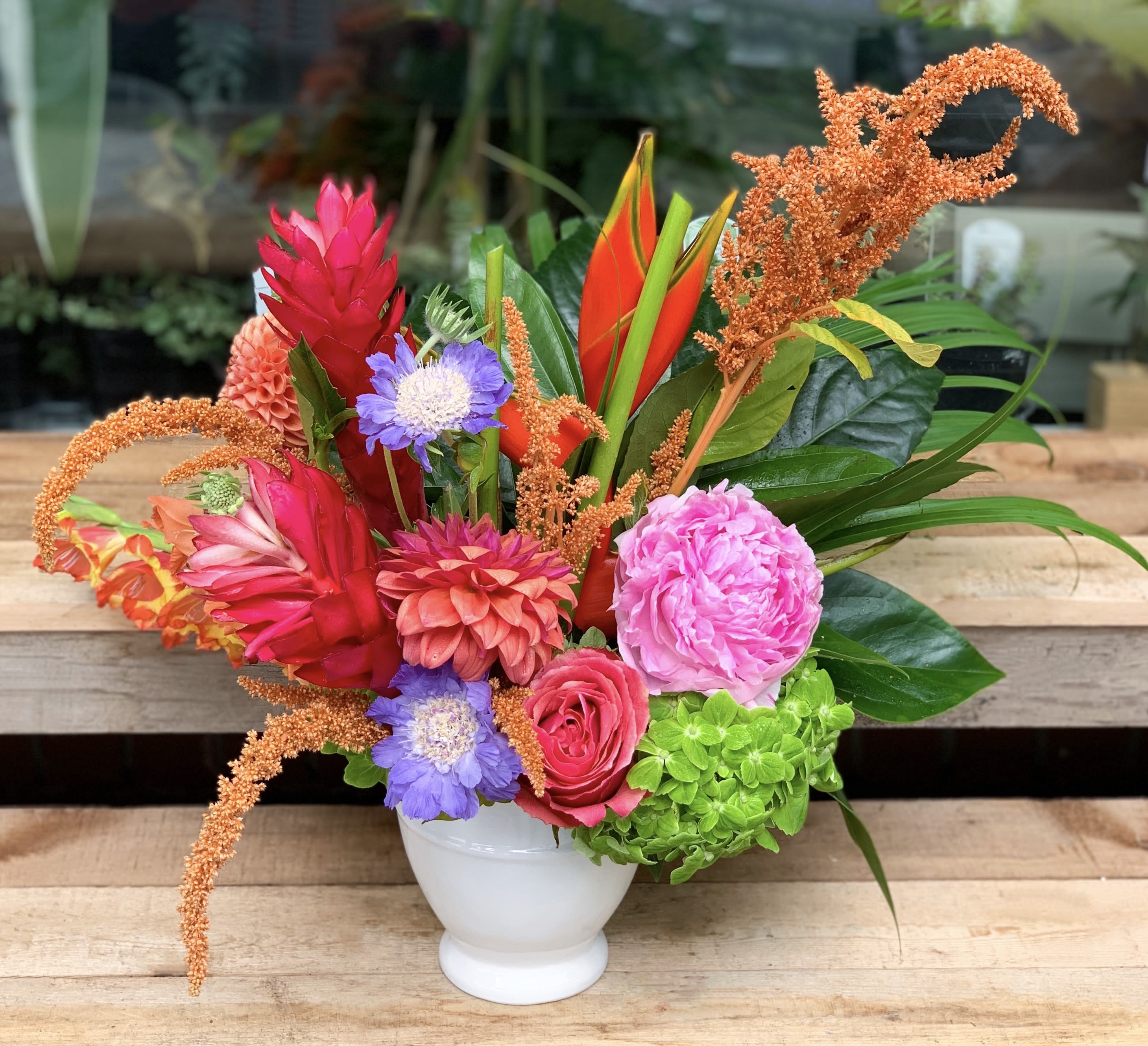 Colorful tropical bouquet in a white vase with pink, orange, purple, and green blooms