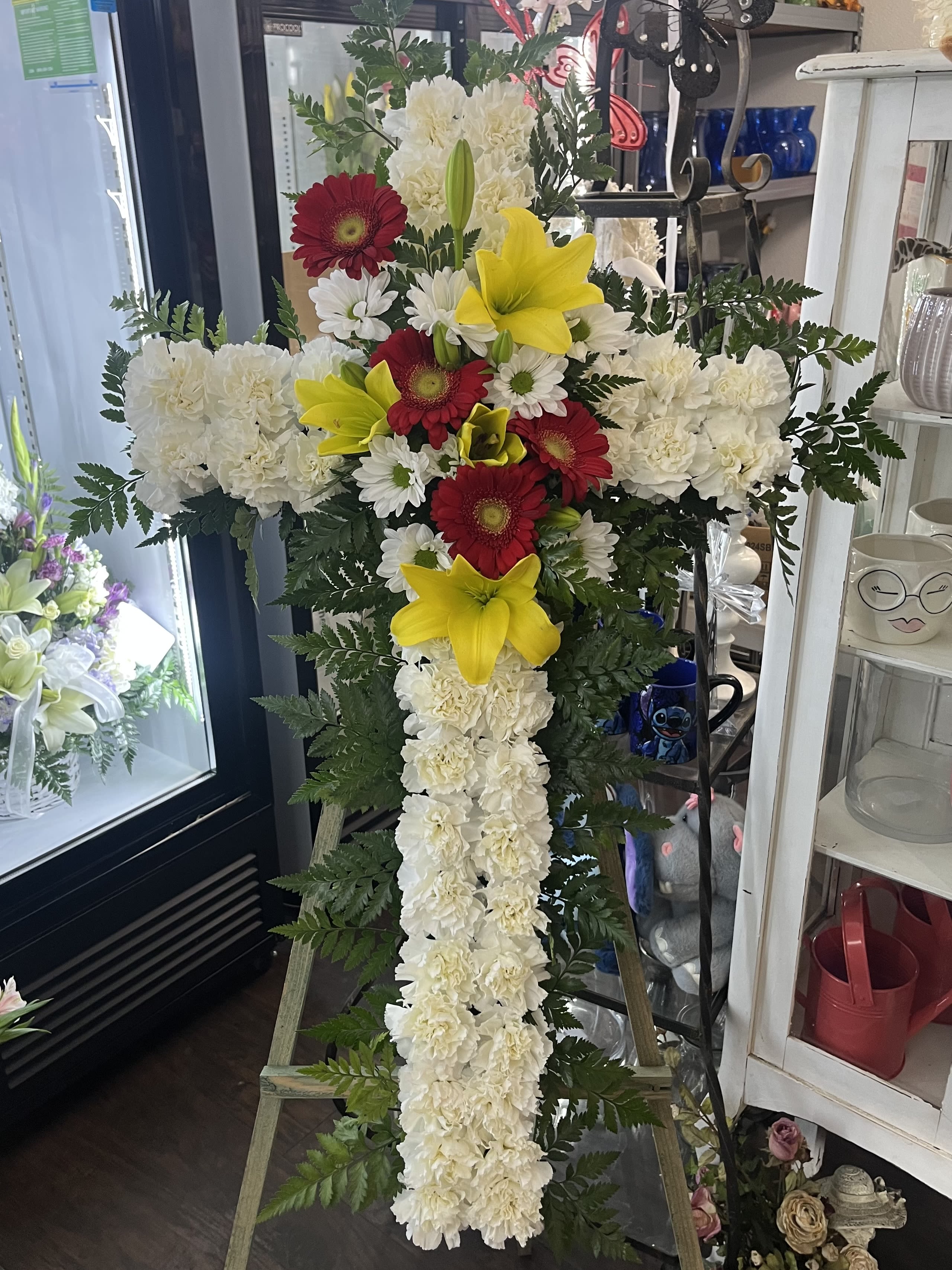 Standing floral cross with white carnations, red gerberas, and yellow lilies
