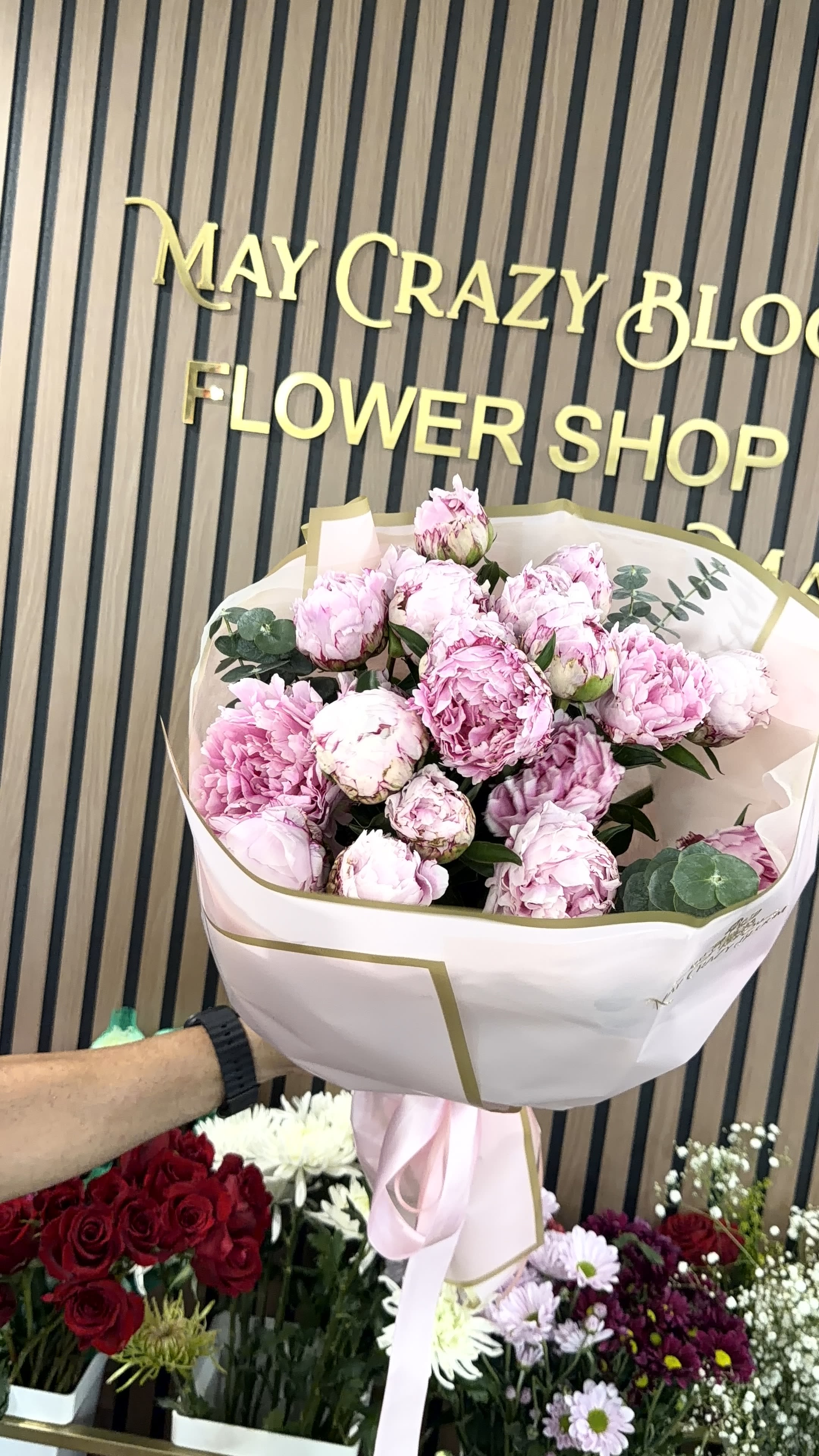 Peonies  - A lush cluster of blush and soft pink peonies creates an immediate romantic impression-perfect as an anniversary bouquet, Mother's Day gift, birthday surprise, or a thoughtful just-because arrangement. The full, layered blooms range from tightly furled buds to wide-open peonies, so the recipient will enjoy changing textures and a gently evolving display as the buds unfurl.  Wrapped in white paper with gold edging and tied with a pale pink satin ribbon, this gift-ready arrangement reads as both elegant and fresh. Small sprigs of eucalyptus-like foliage add muted green contrast that highlights the pastel petals without competing with them. The presentation includes decorative paper wrap and a soft pink ribbon for a polished finish.  This bouquet is designed to make someone feel truly seen-romantic, celebrated, and appreciated. Arrange delivery for the special day and remind recipients to recut stems and change the water every other day to prolong vase life.