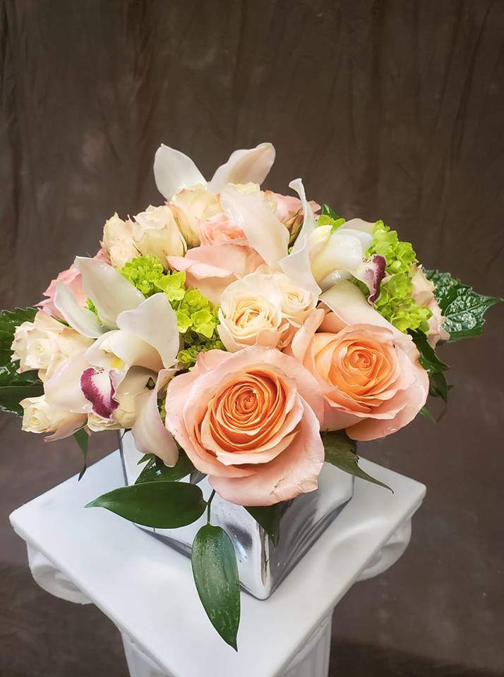 Peach roses and white orchids in a square glass vase
