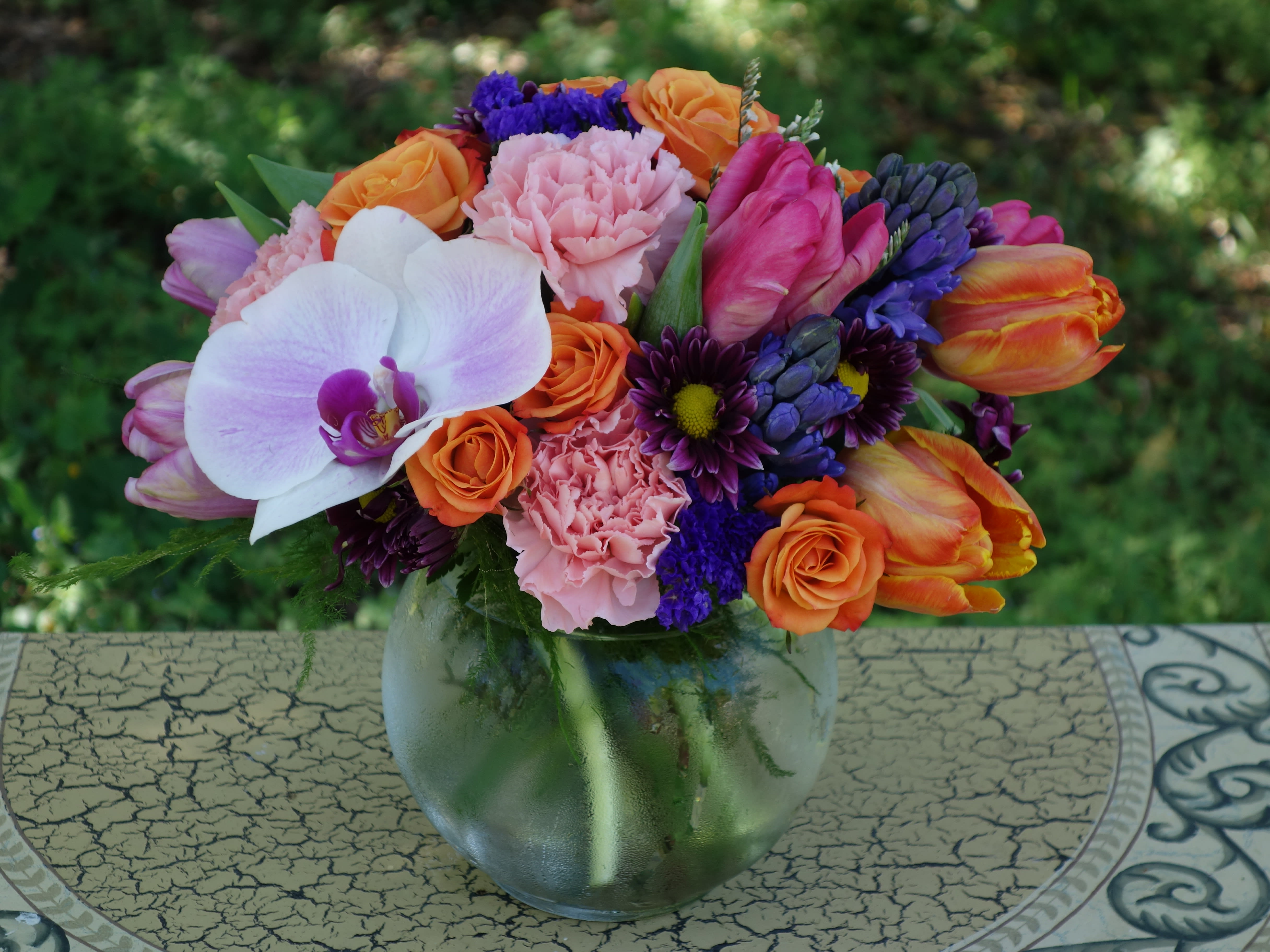 Colorful mixed bouquet with orchid, roses, tulips, and carnations in a round glass vase