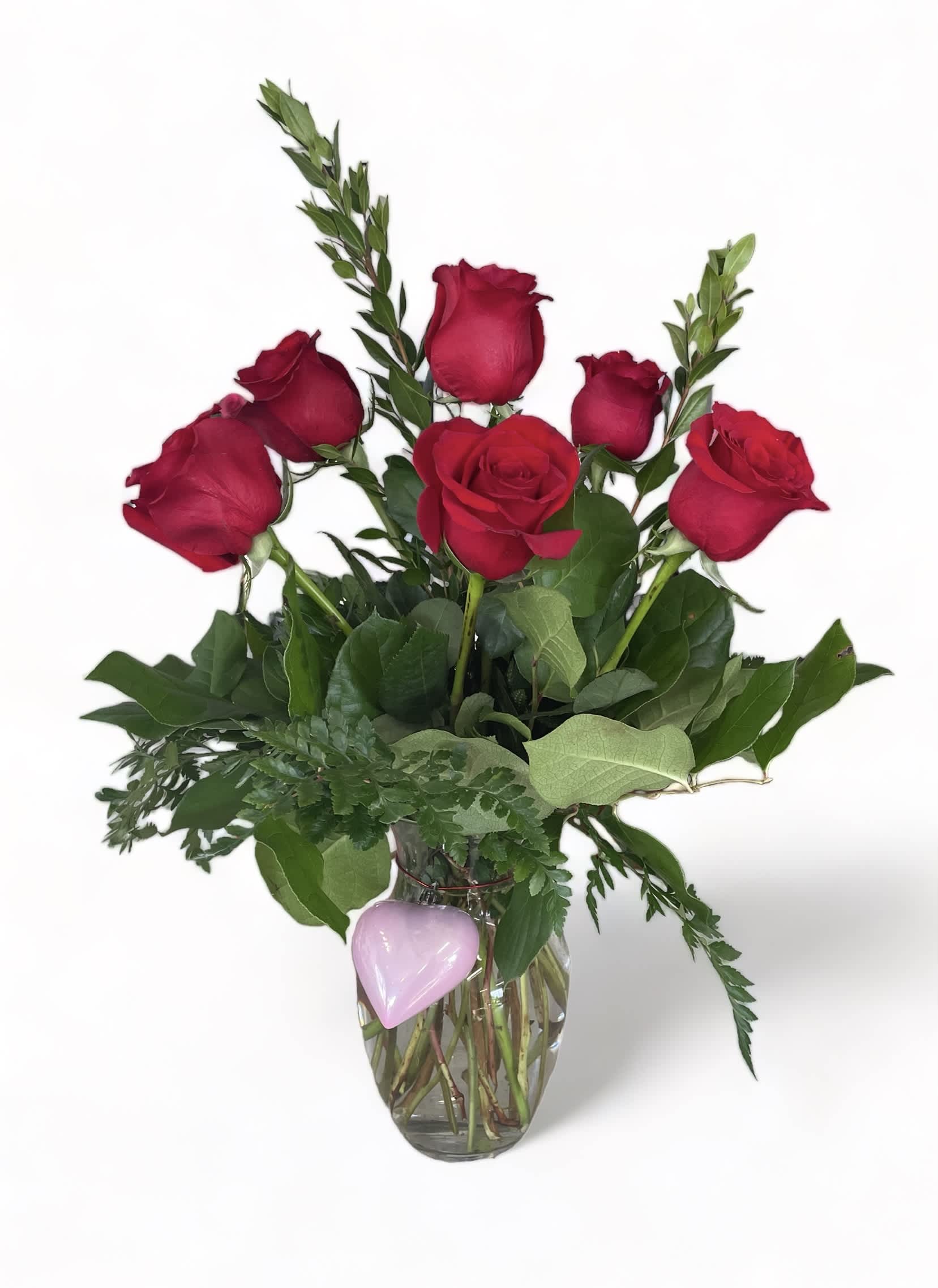 Red roses in a clear glass vase with a pink heart decoration