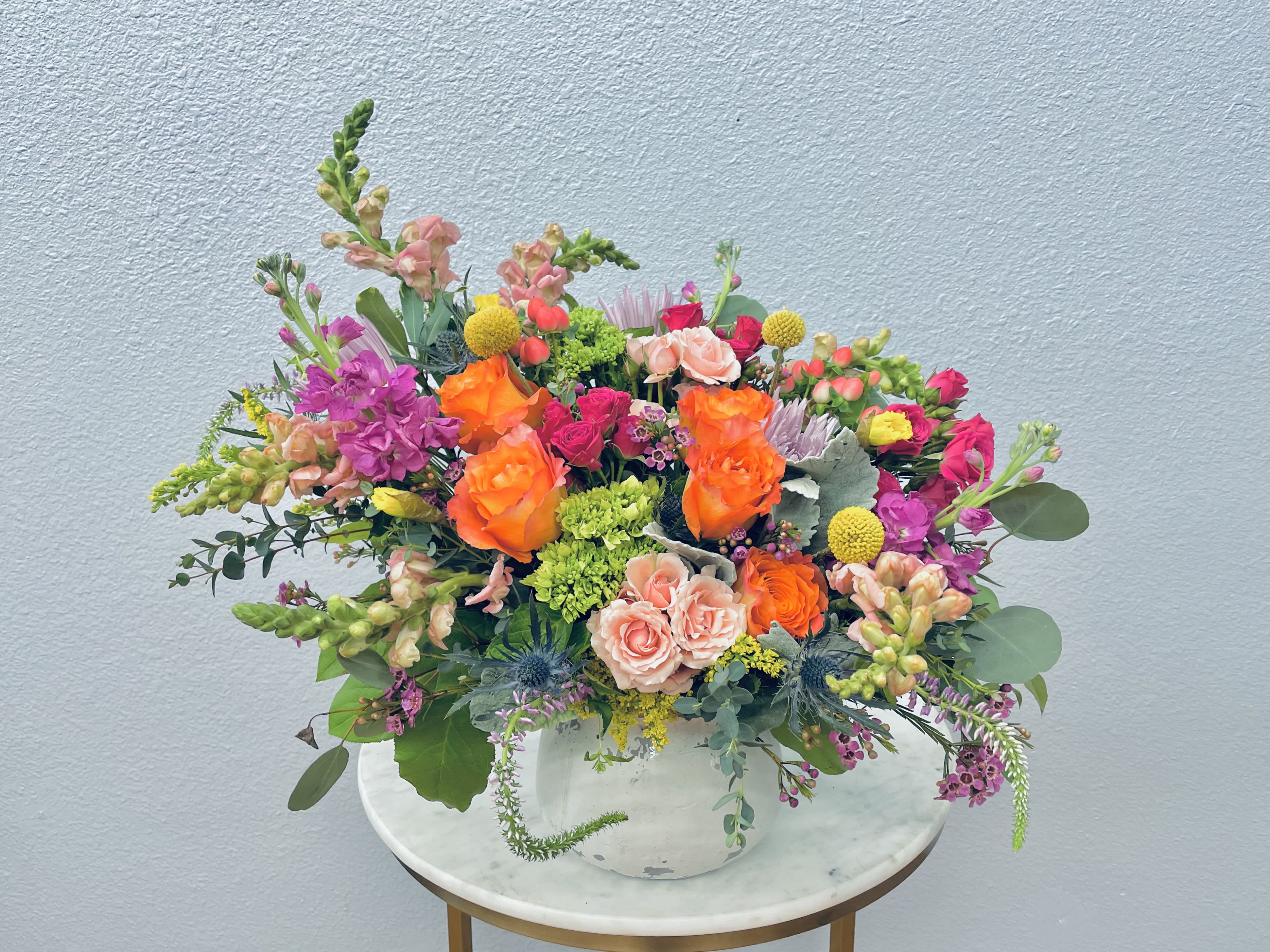 Mixed bouquet of orange, pink, and purple flowers in a white vase