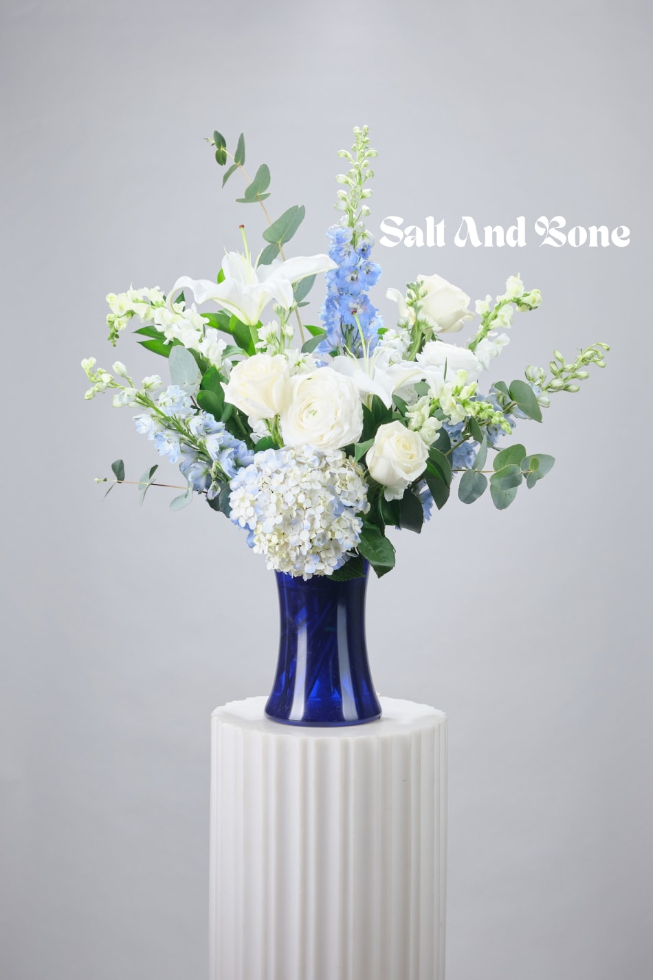 White and blue floral arrangement in a cobalt vase