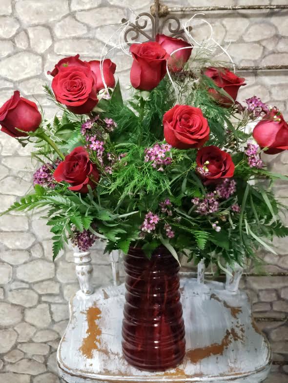 Tall arrangement of red roses with small pink blossoms in a red glass vase