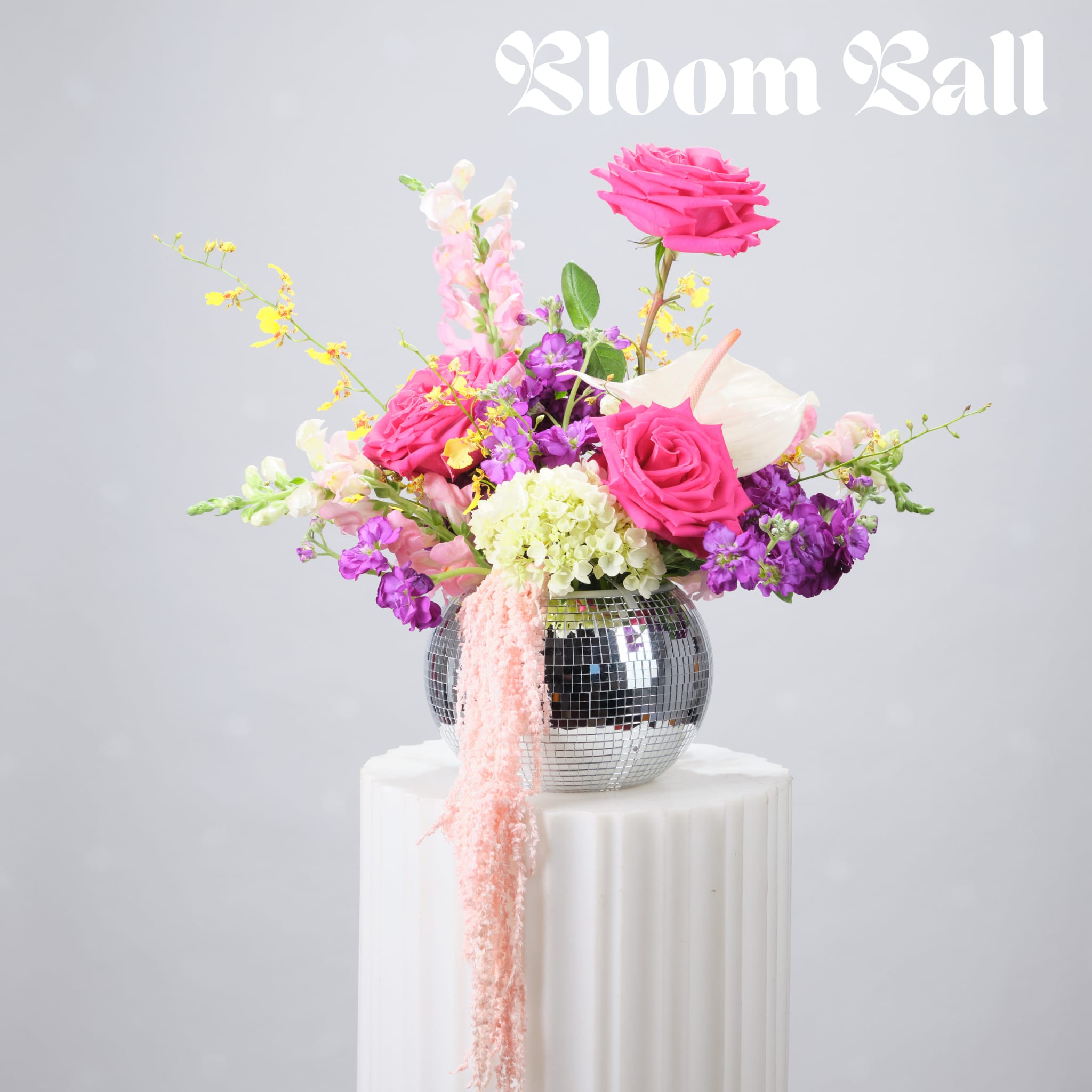 Bright pink and purple floral arrangement in a mirrored vase on a white pedestal