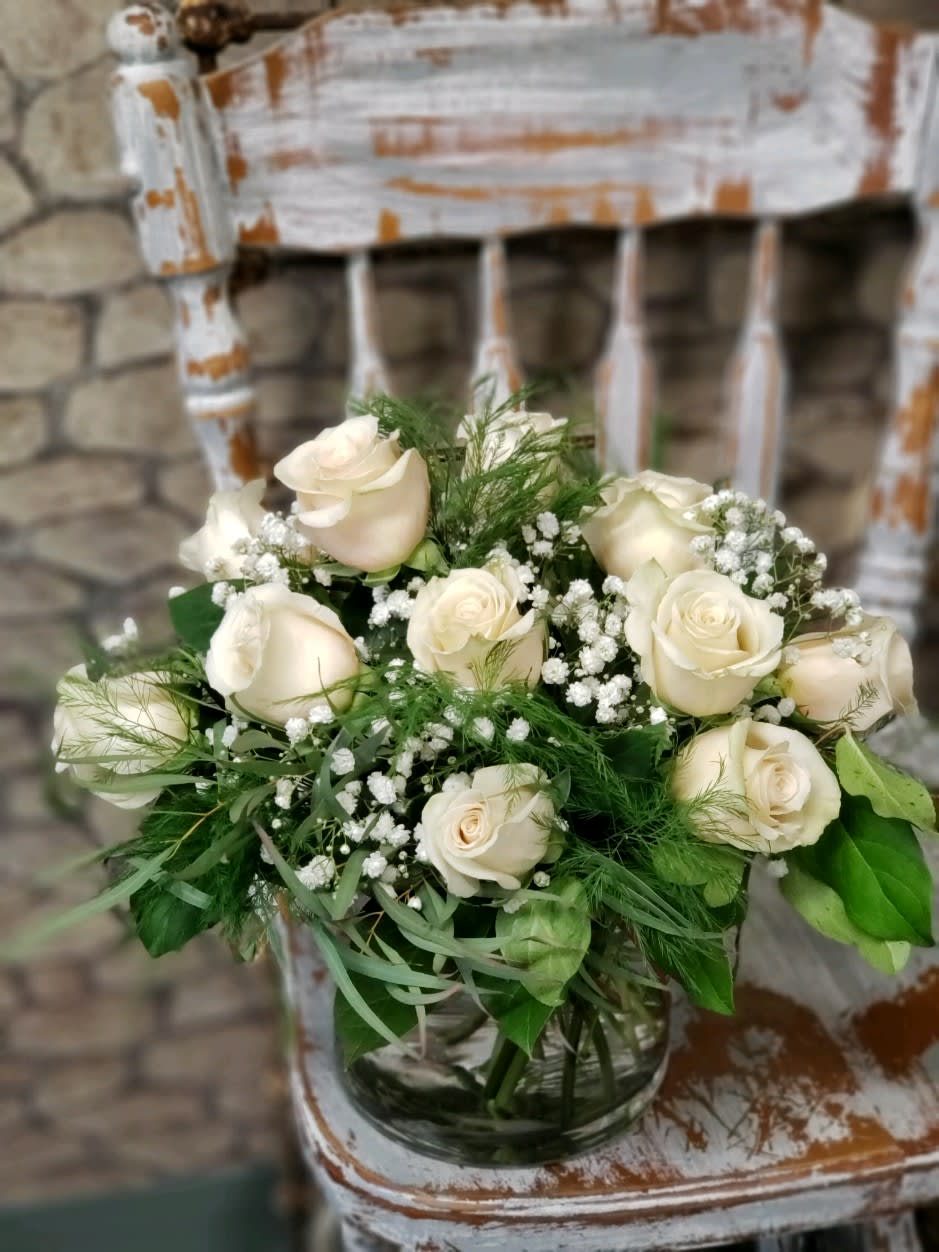 Round arrangement of ivory roses and baby's breath in a glass vase on a rustic white chair