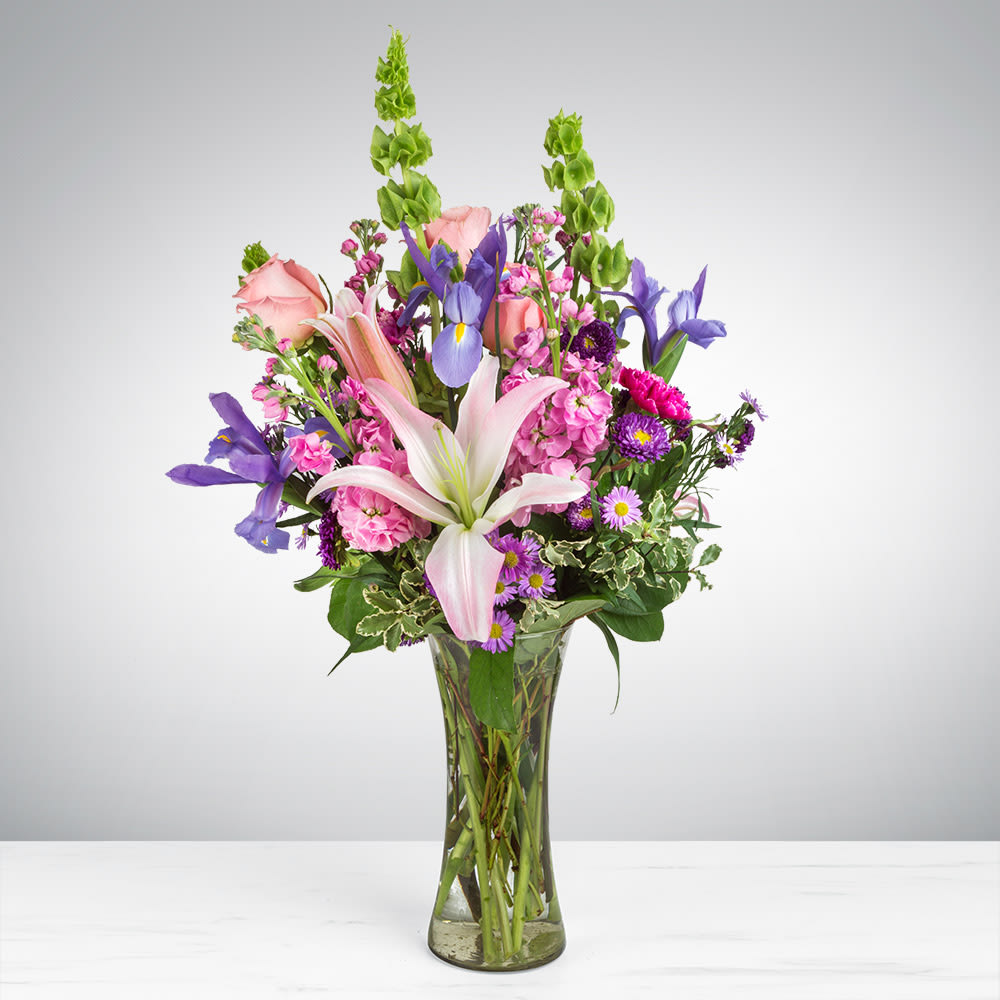 Mixed bouquet of pink, purple, and white flowers in a clear glass vase