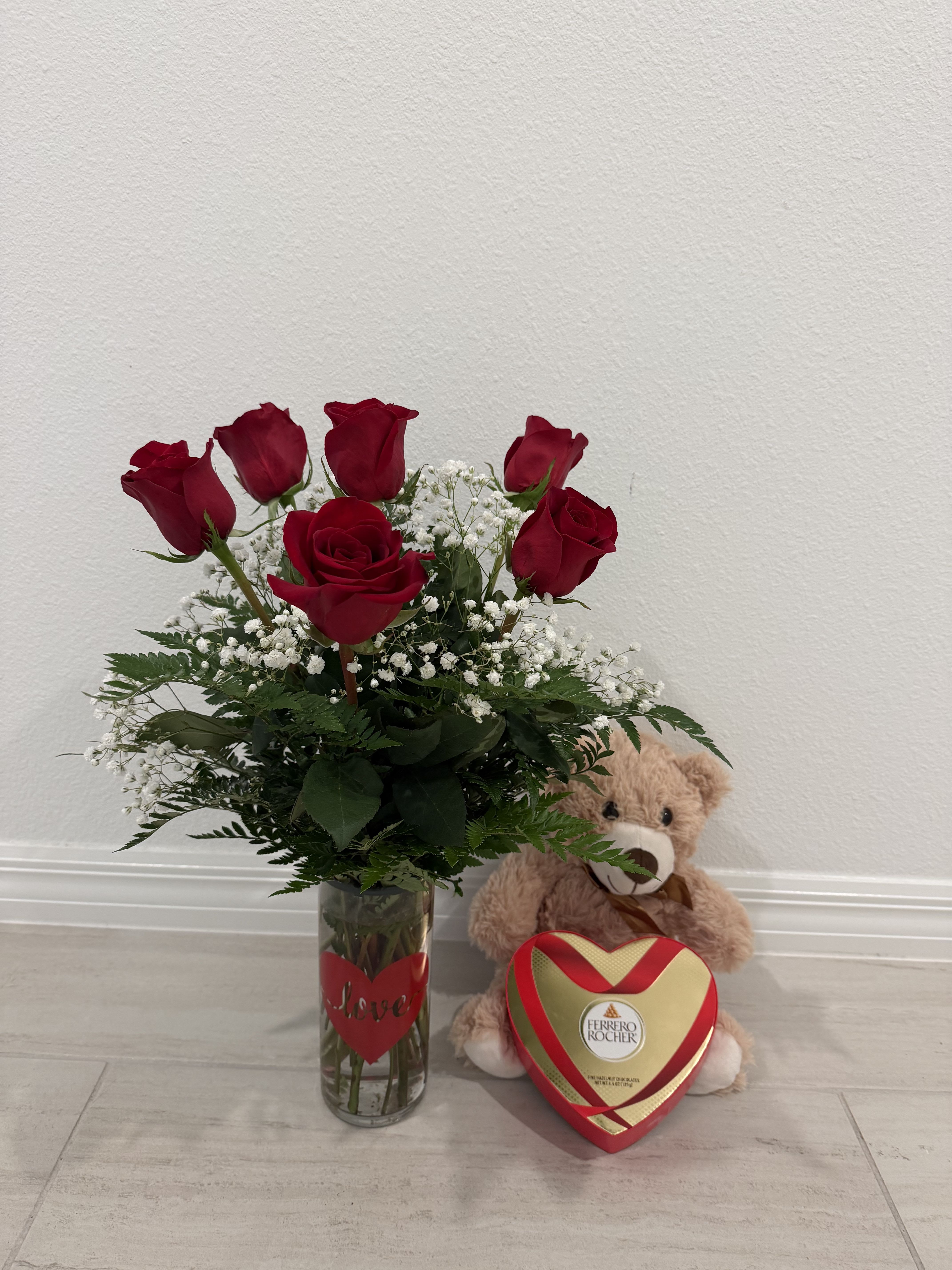 Red roses in a glass vase with a teddy bear and heart-shaped chocolate box