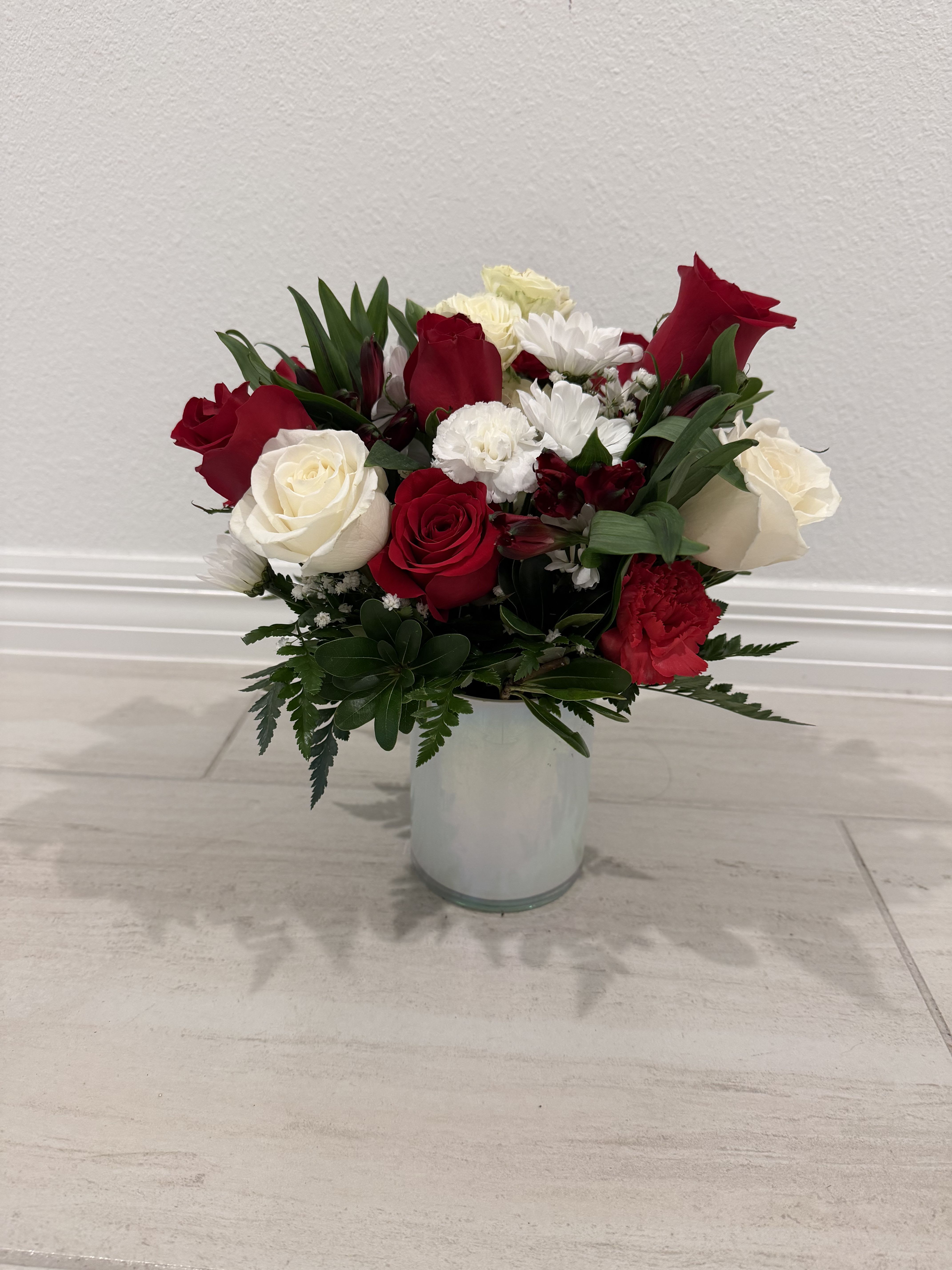 Red and white roses with white daisies in a clear glass vase