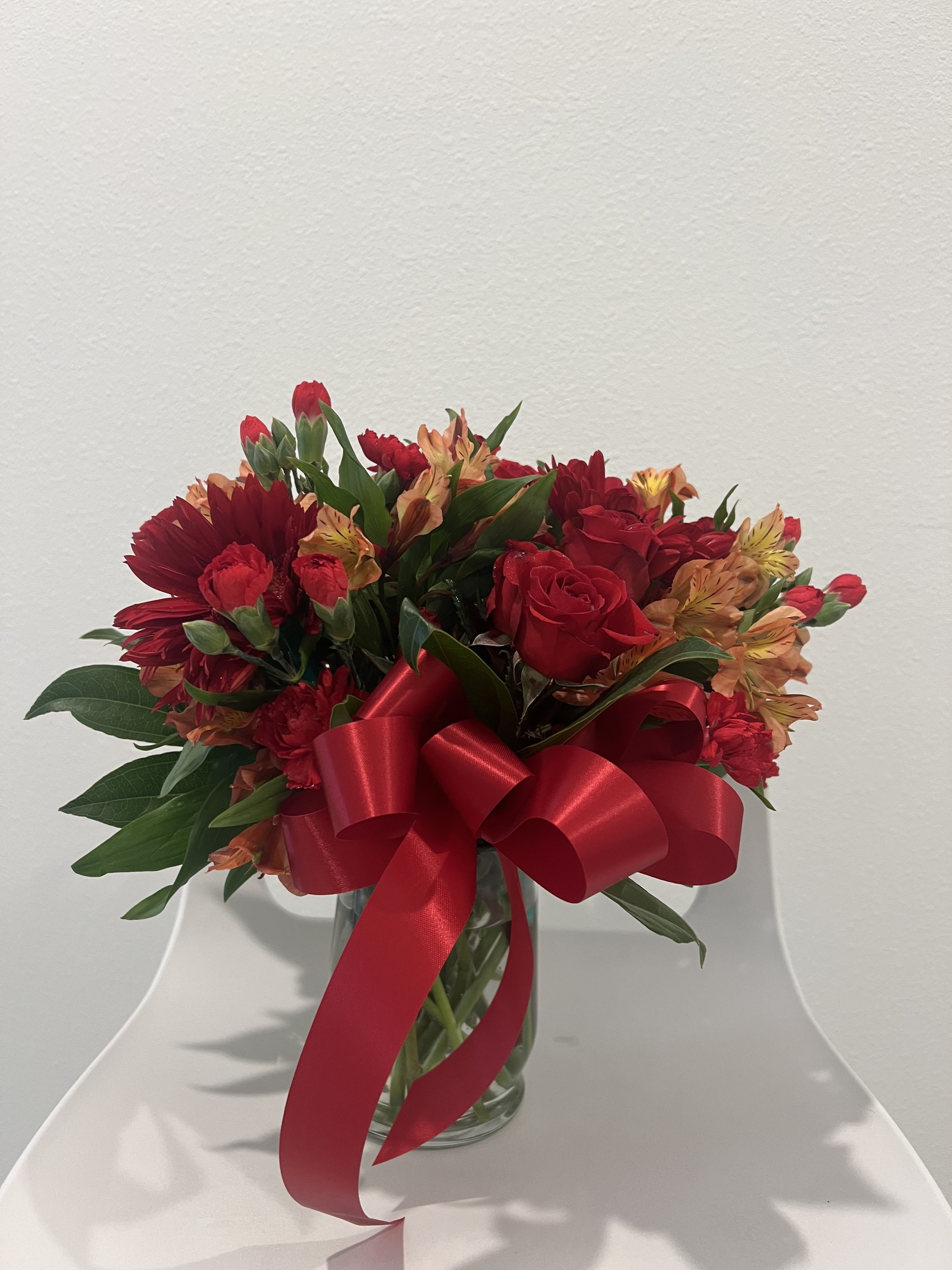 Red and orange mixed bouquet in a glass vase with a large red ribbon