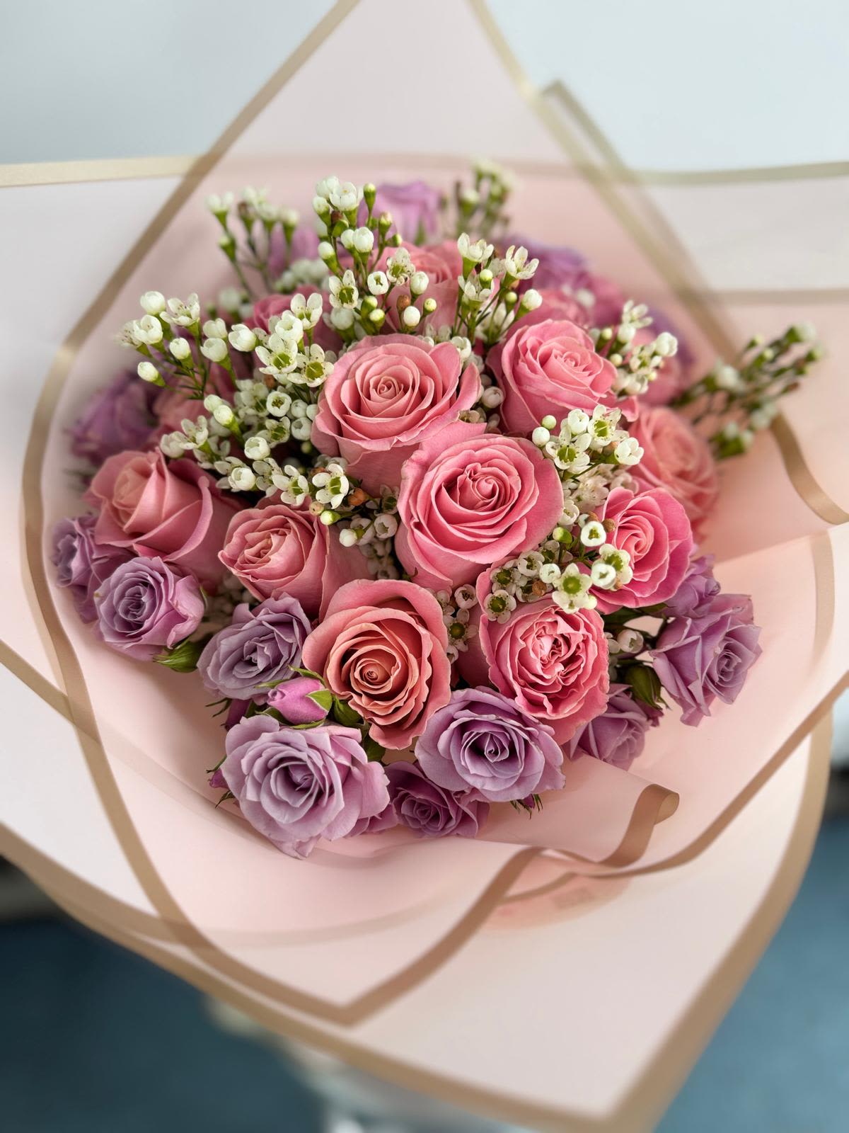 Bouquet of pink and lavender roses wrapped in pale pink paper