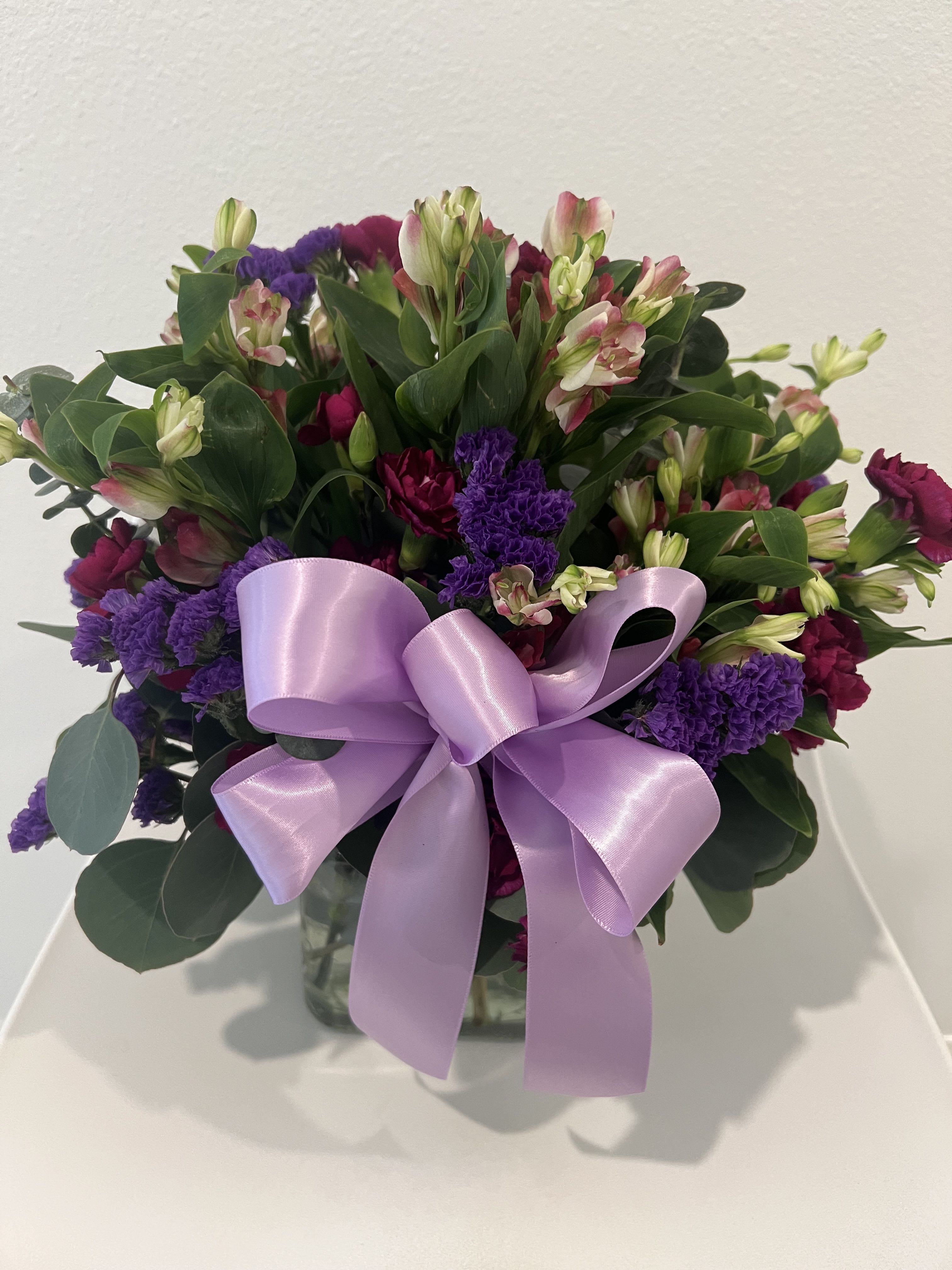Bouquet of pink and purple flowers with a lavender ribbon in a glass vase