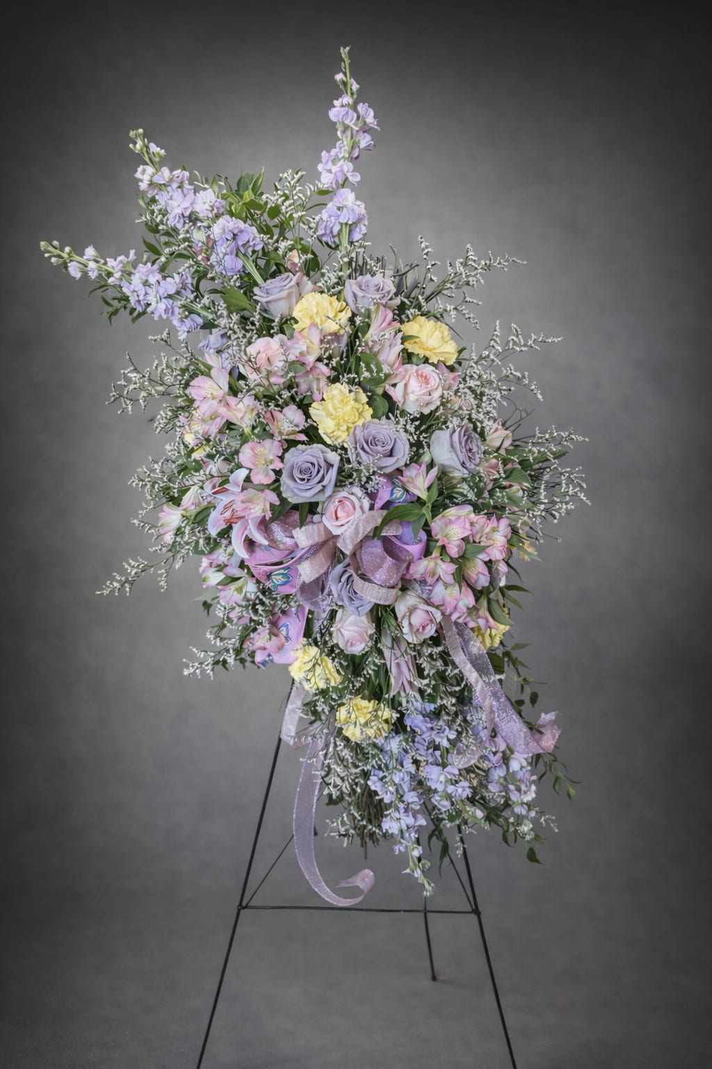 Large pastel floral standing spray with roses, lilies, and ribbons on an easel