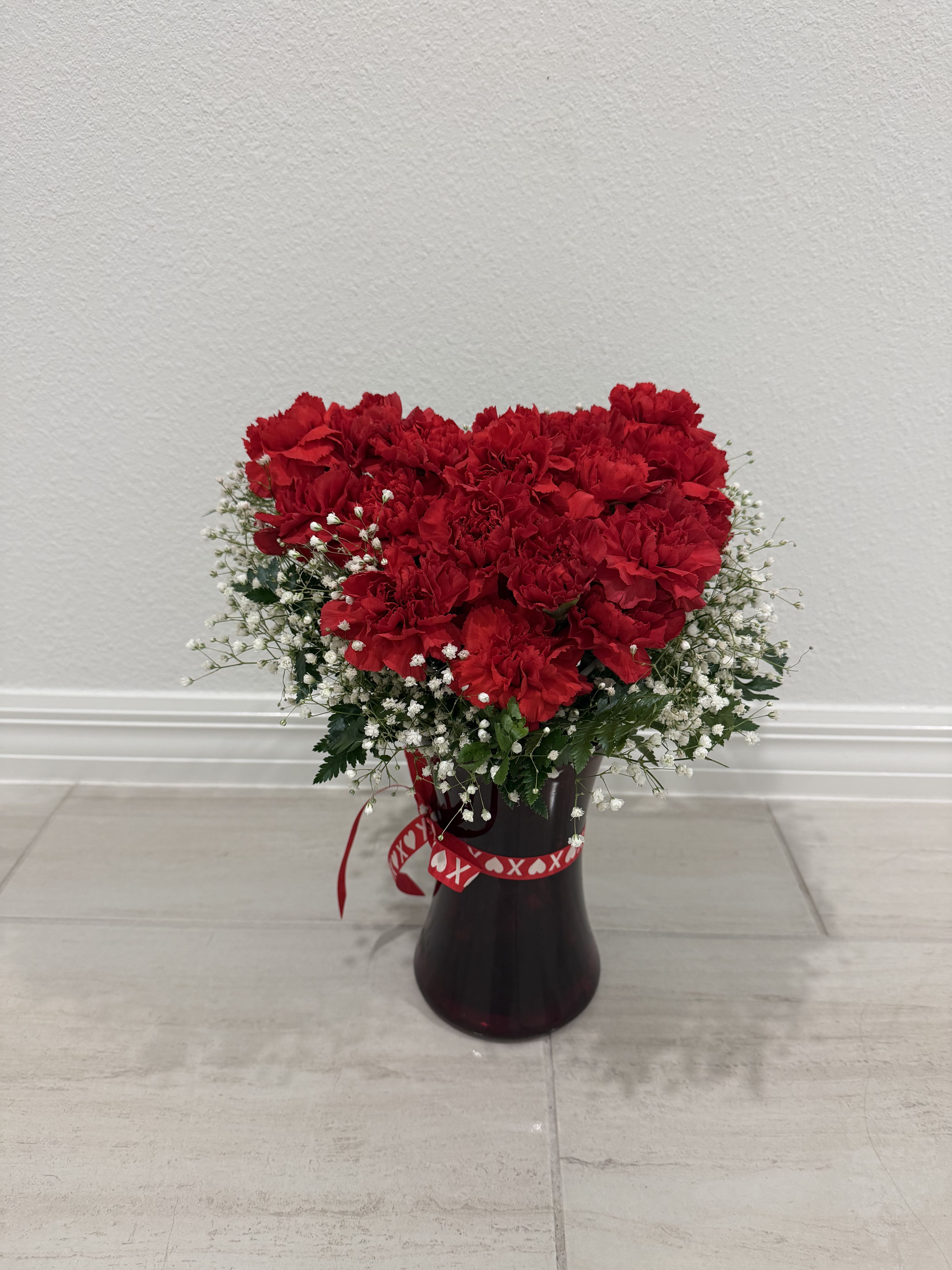Red carnations arranged in a dark vase with white baby's breath