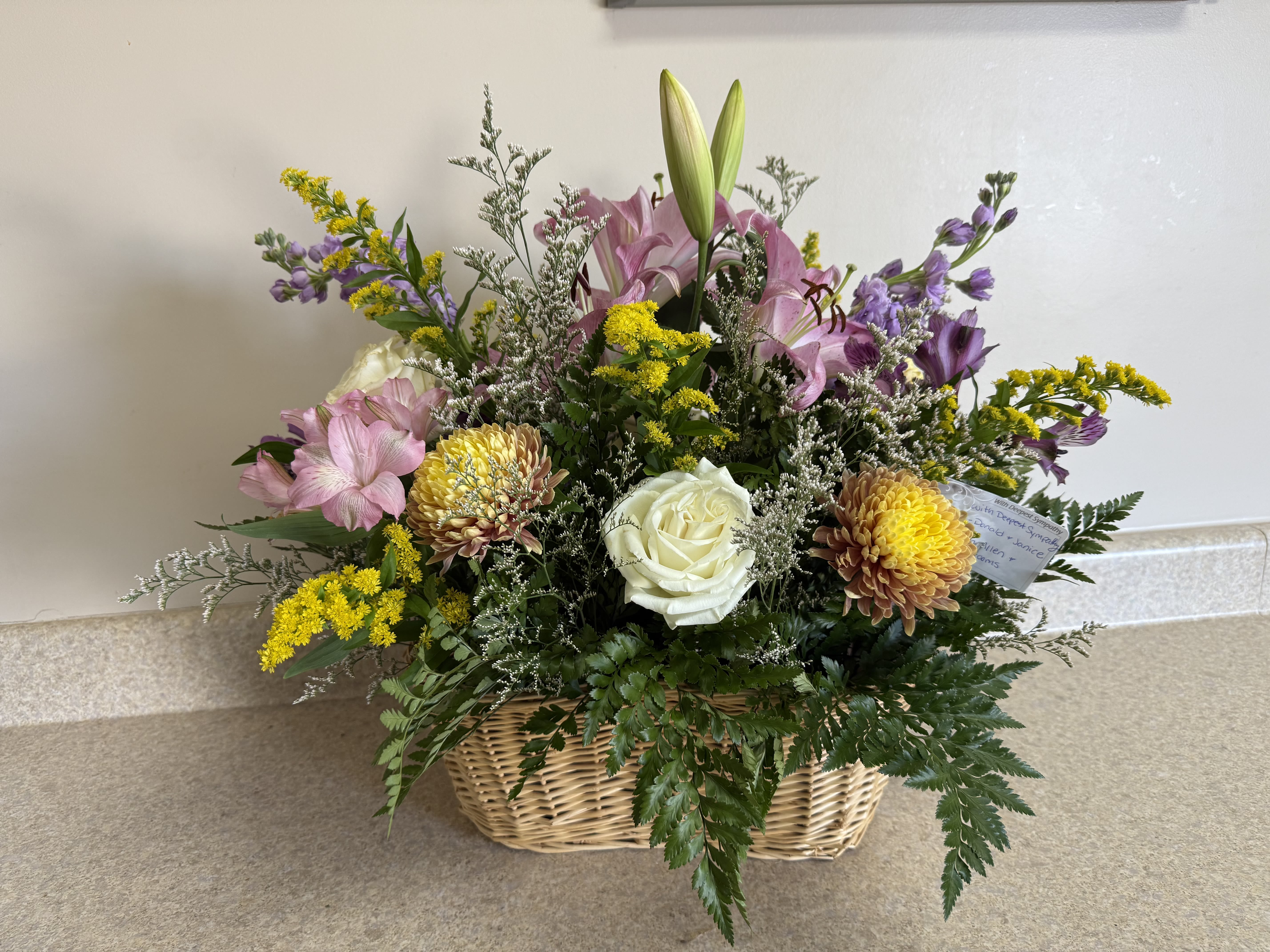 Mixed bouquet in a wicker basket with pink lilies, white roses, and yellow flowers