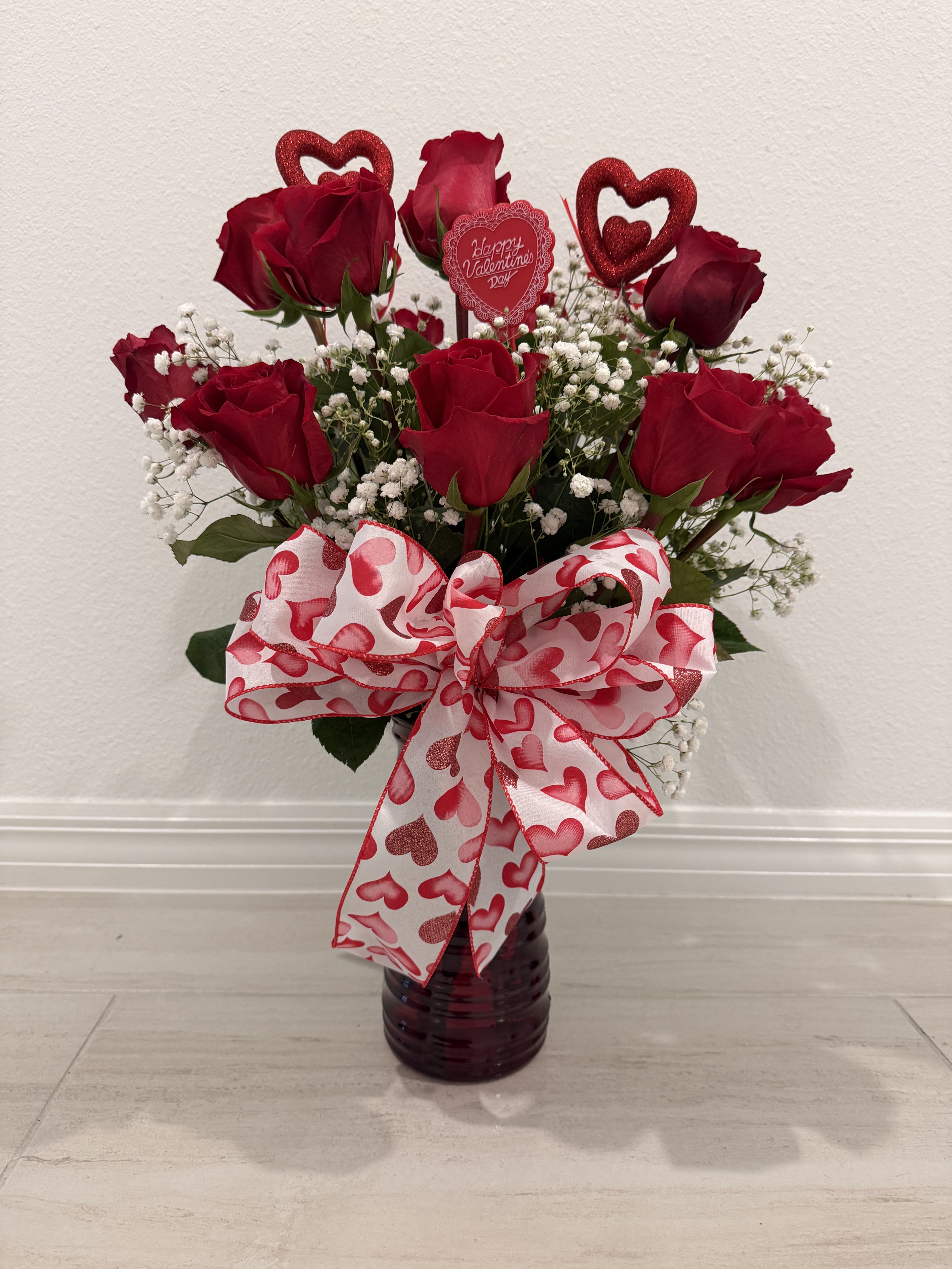 Red roses in a dark vase with a heart-patterned bow and Valentine topper