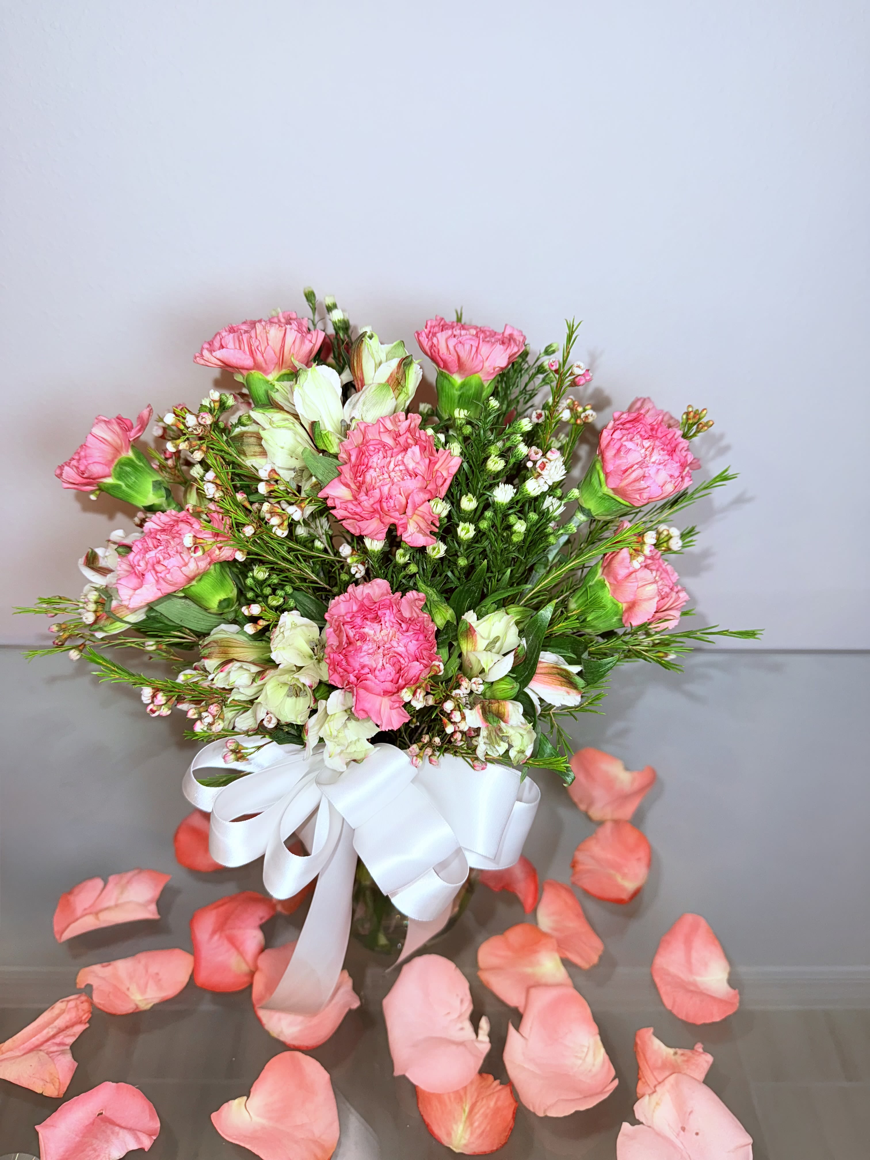 Pink carnations and white blooms in a vase with a white ribbon