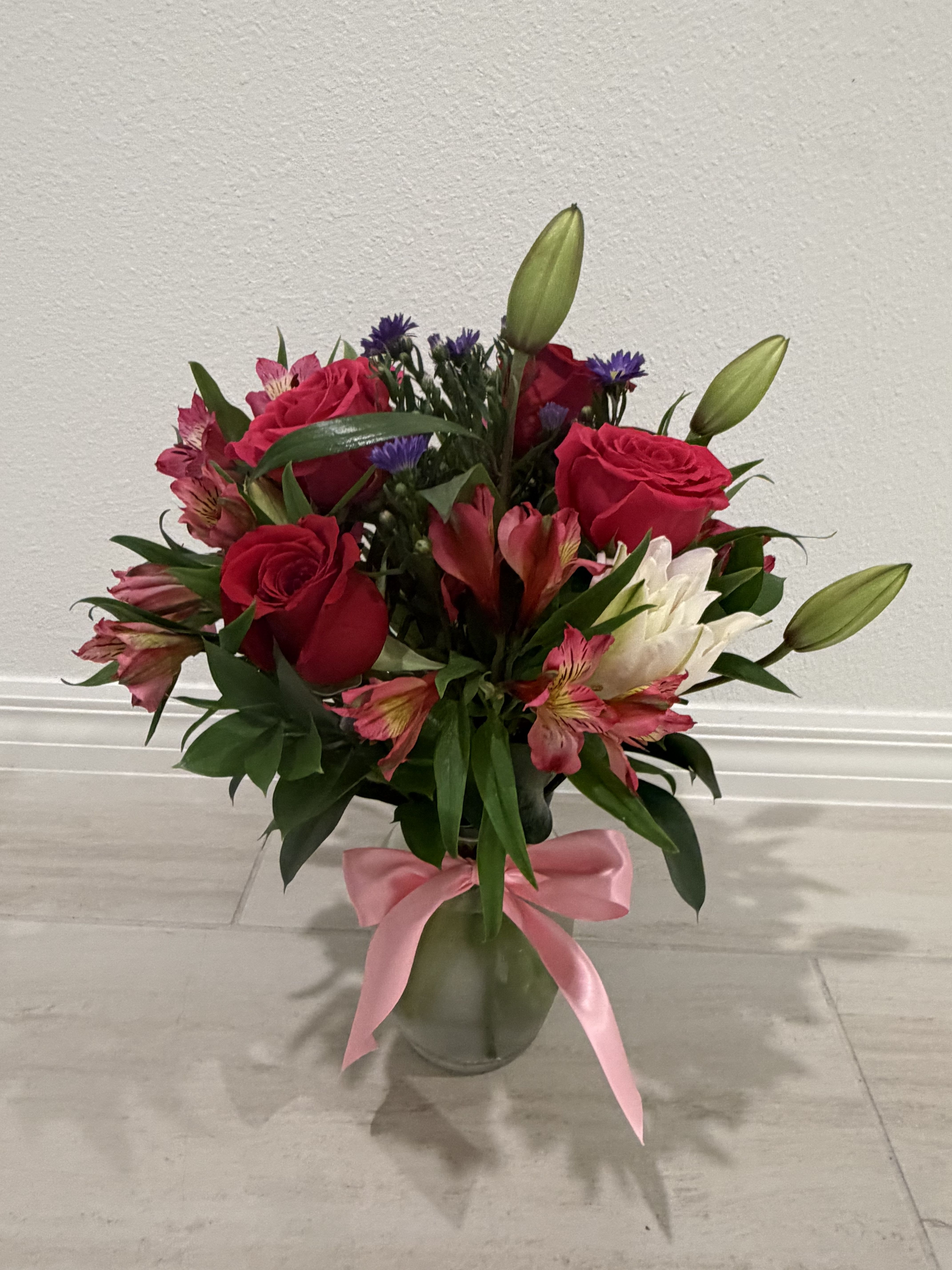 Bouquet of red roses, lilies, and pink flowers in a glass vase with a pink ribbon