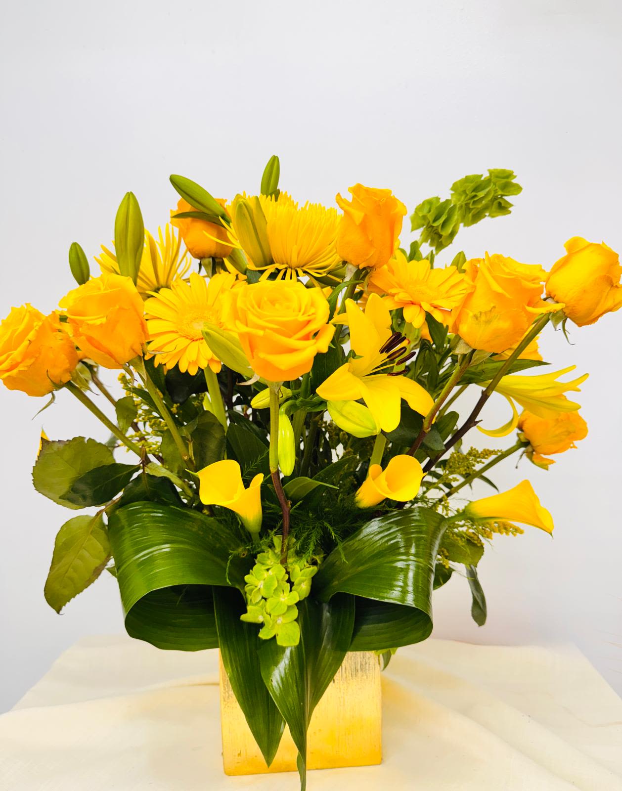 Yellow roses, lilies, and daisies in a square vase