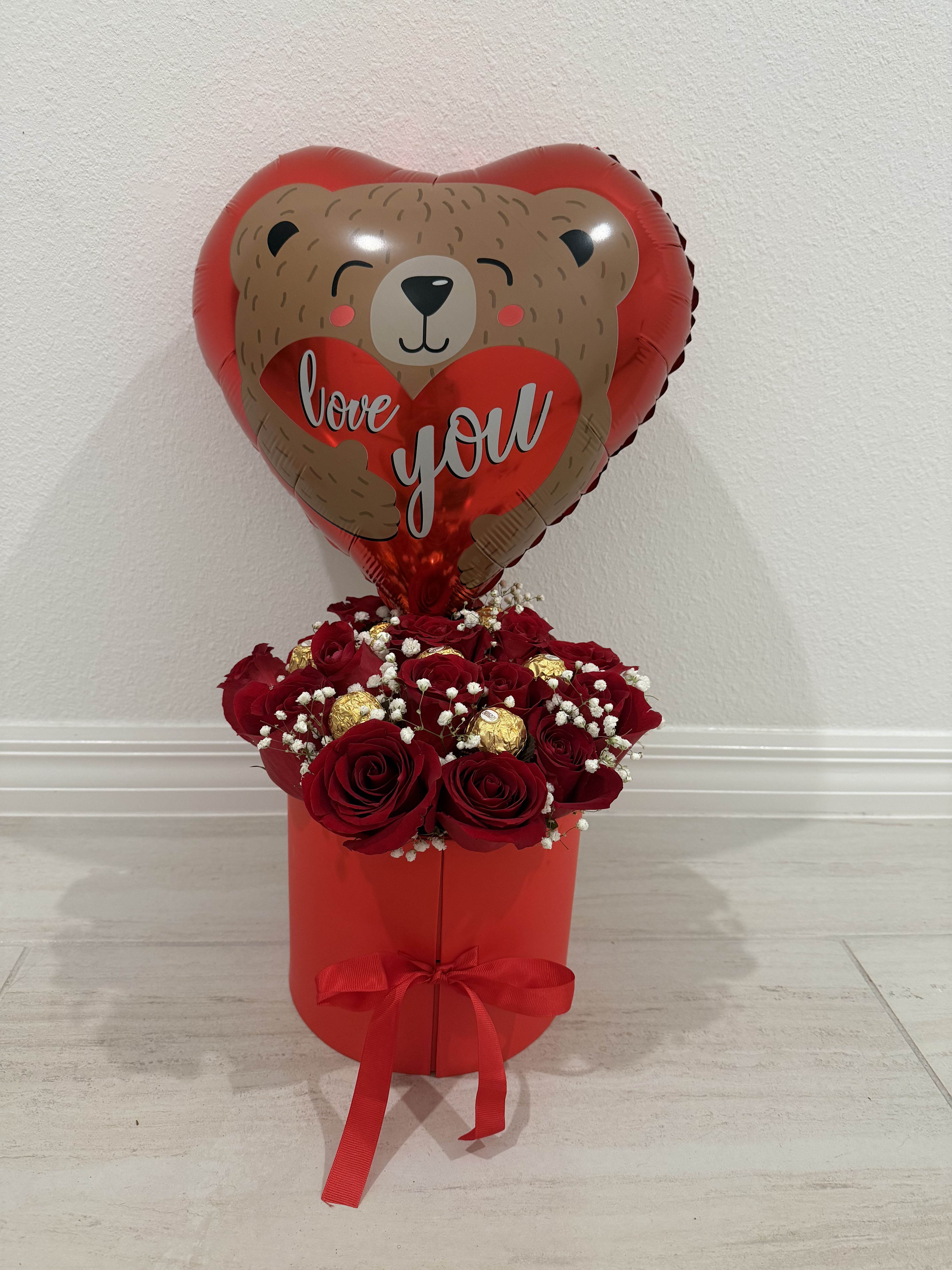 Red rose arrangement in a red box with a heart-shaped teddy bear balloon