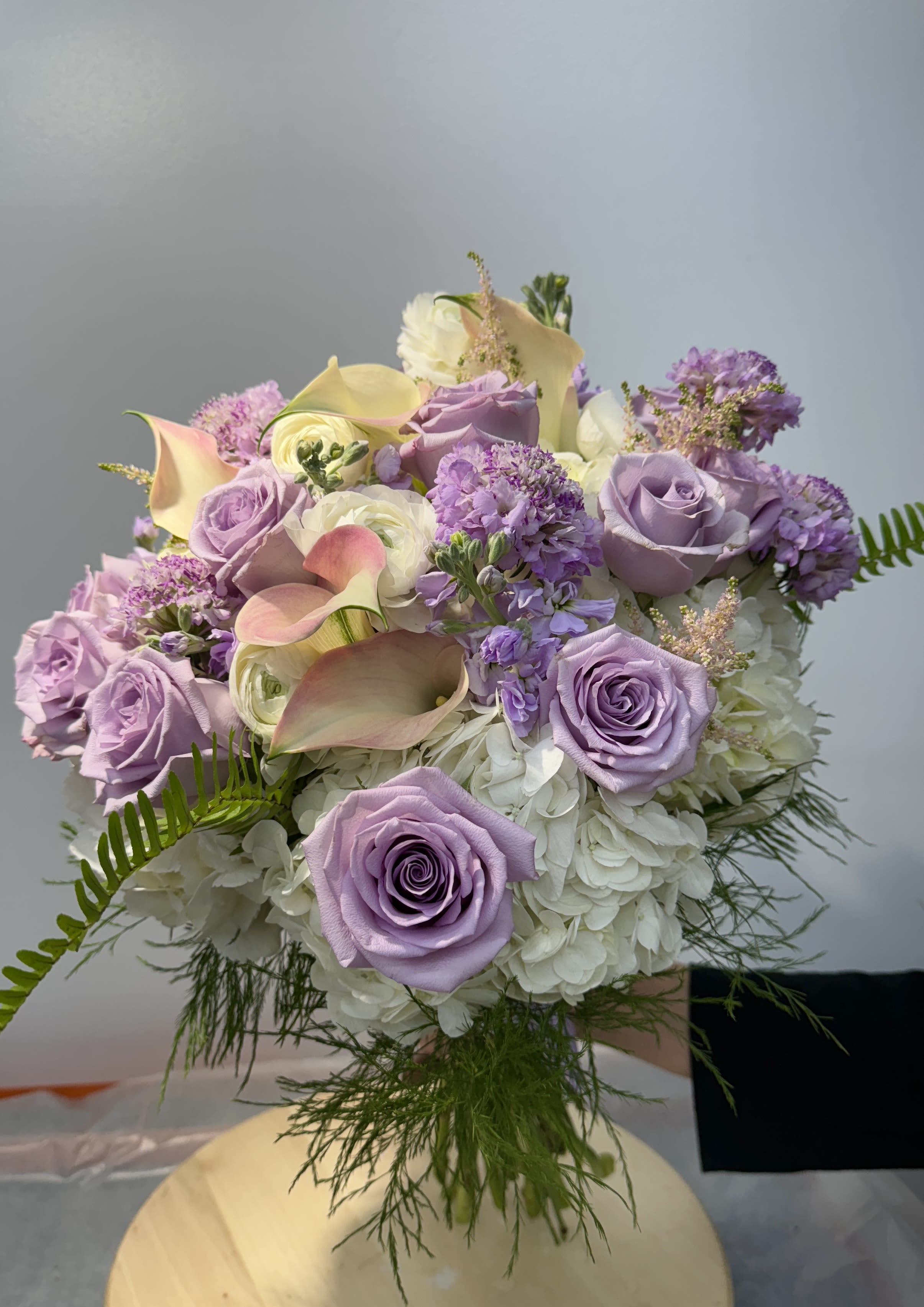 Lavender roses and calla lilies arranged with white hydrangeas.
