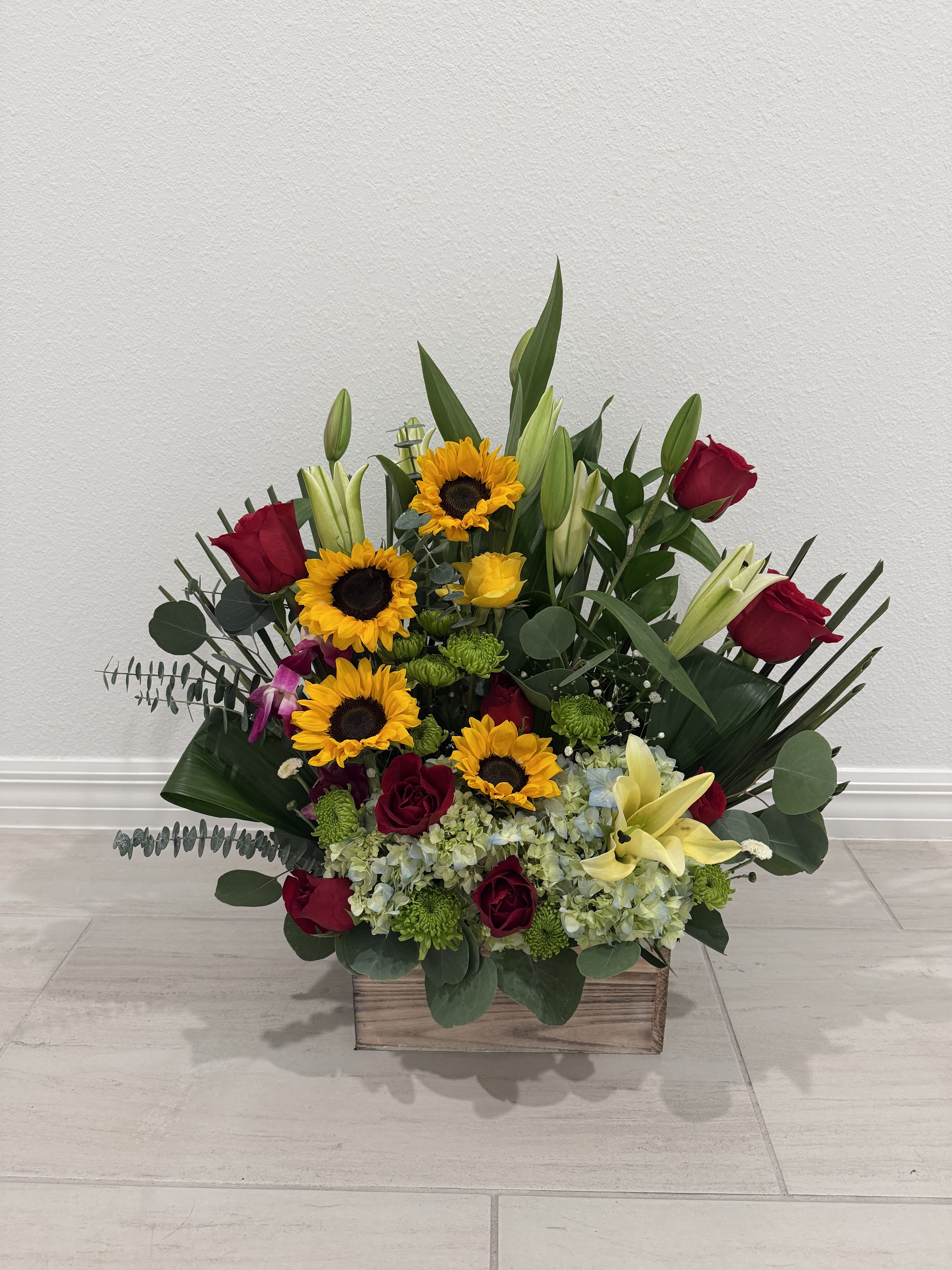 Mixed bouquet with sunflowers, red roses, and lilies in a wooden box