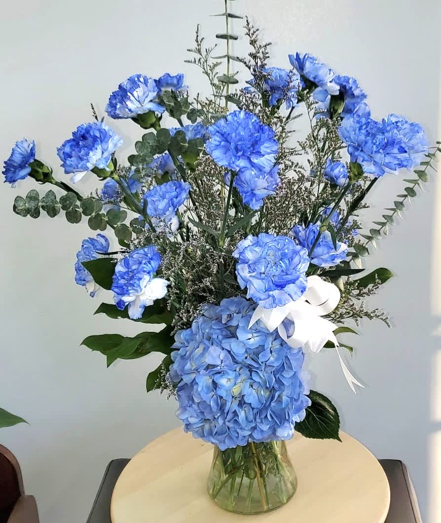 Blue carnations and hydrangea in a glass vase with a white ribbon