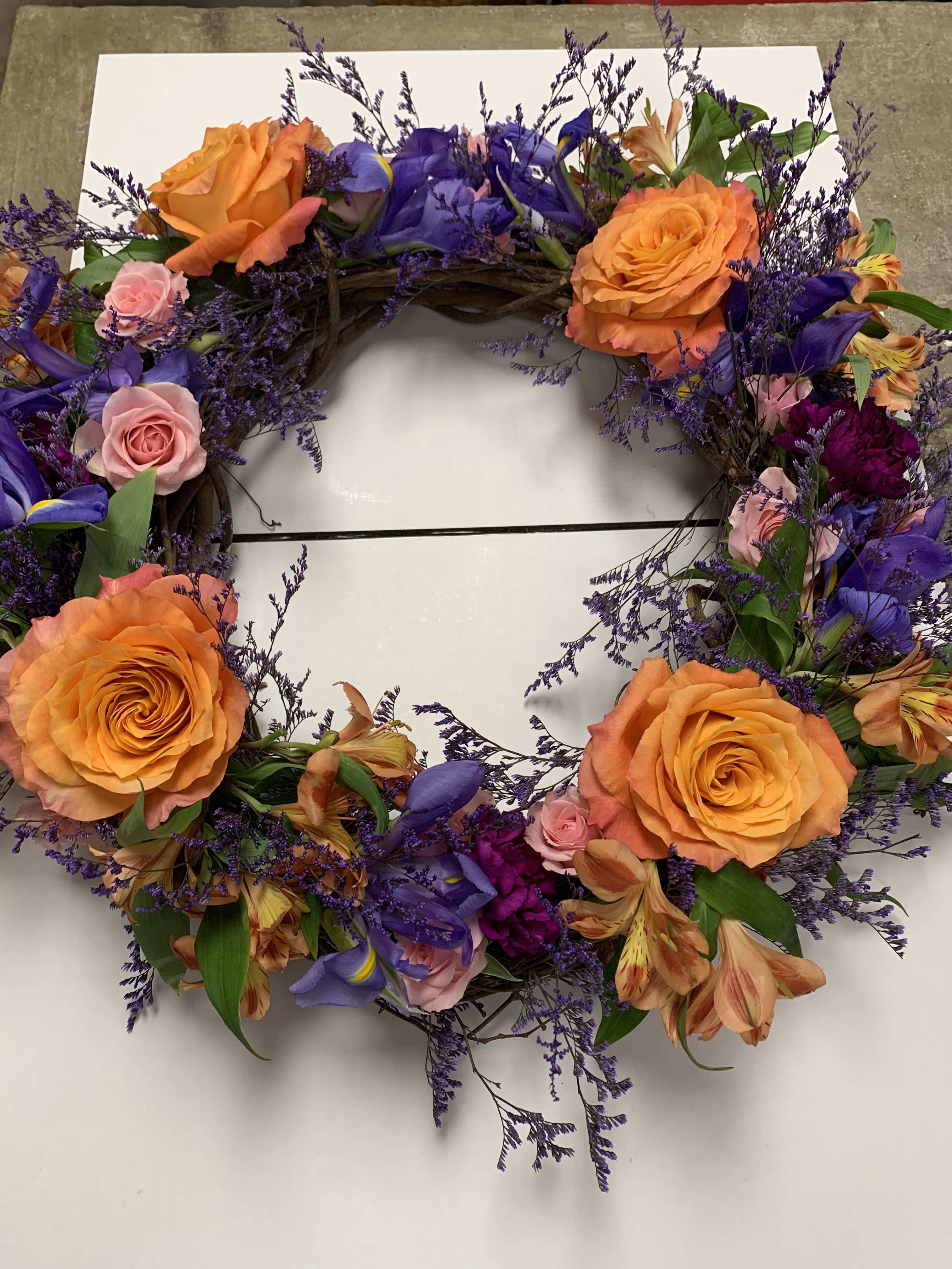 Circular floral wreath with orange roses, purple flowers, and pink accents