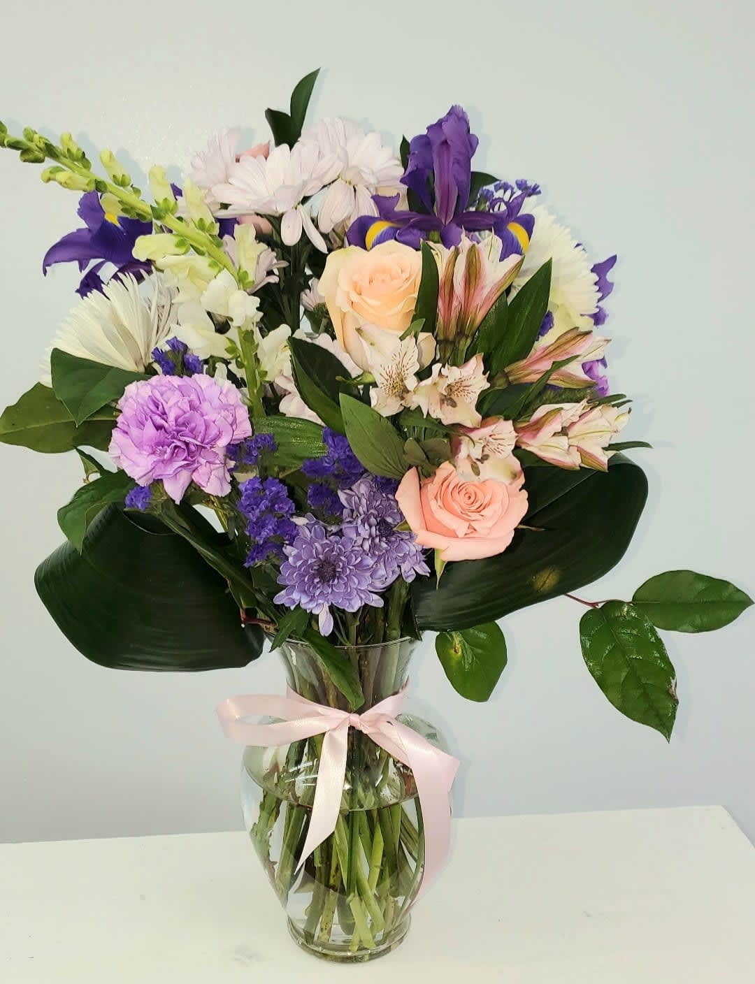 Mixed bouquet of pastel flowers in a clear glass vase with a pink ribbon