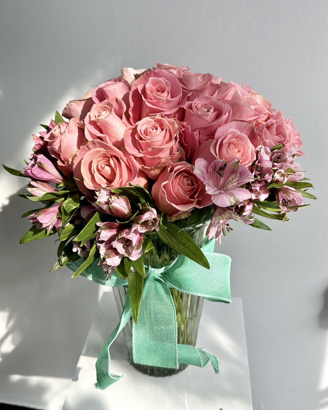 Pink rose bouquet in a glass vase with a turquoise ribbon