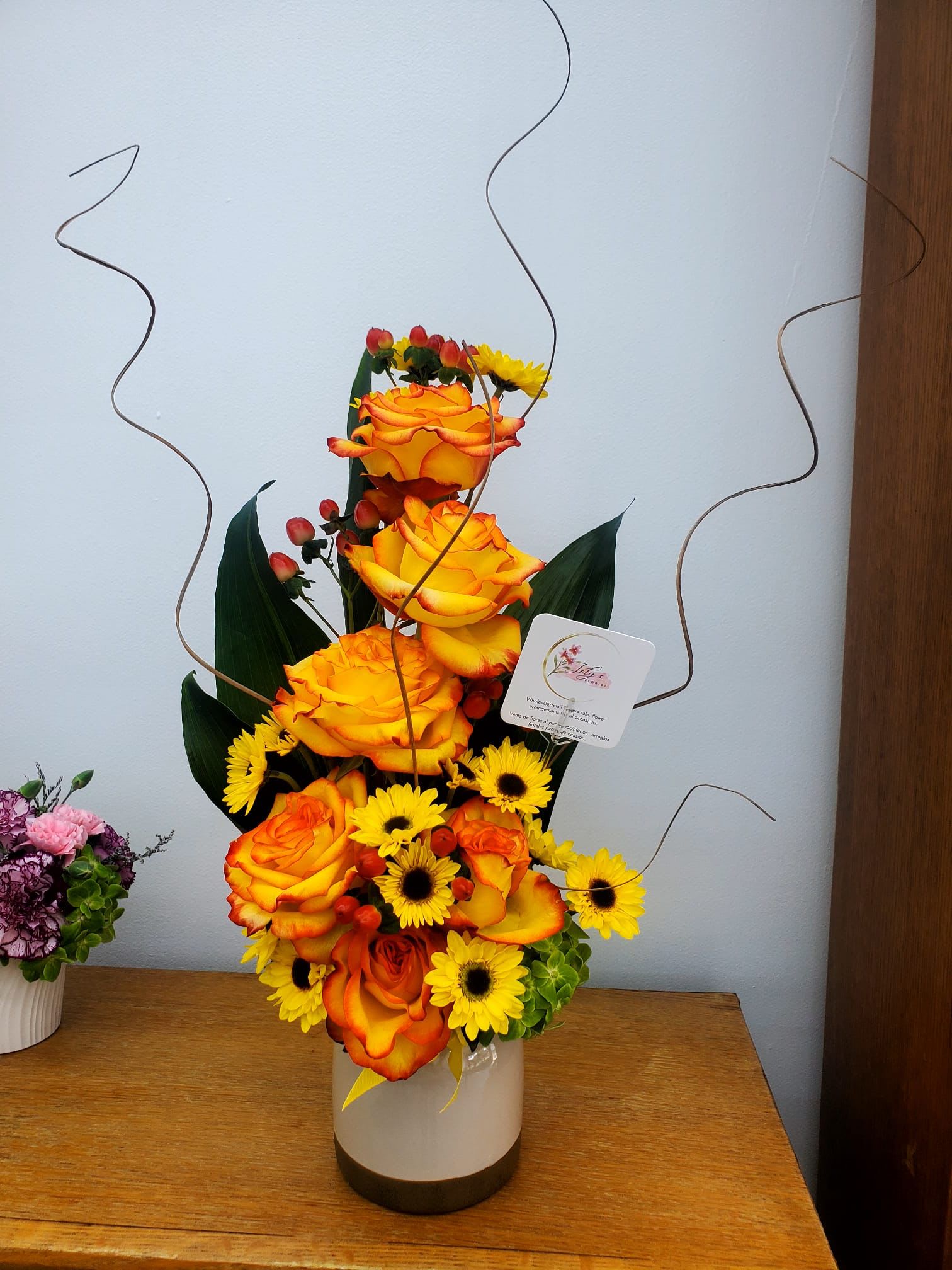 Tall arrangement of orange roses and yellow daisies in a white vase