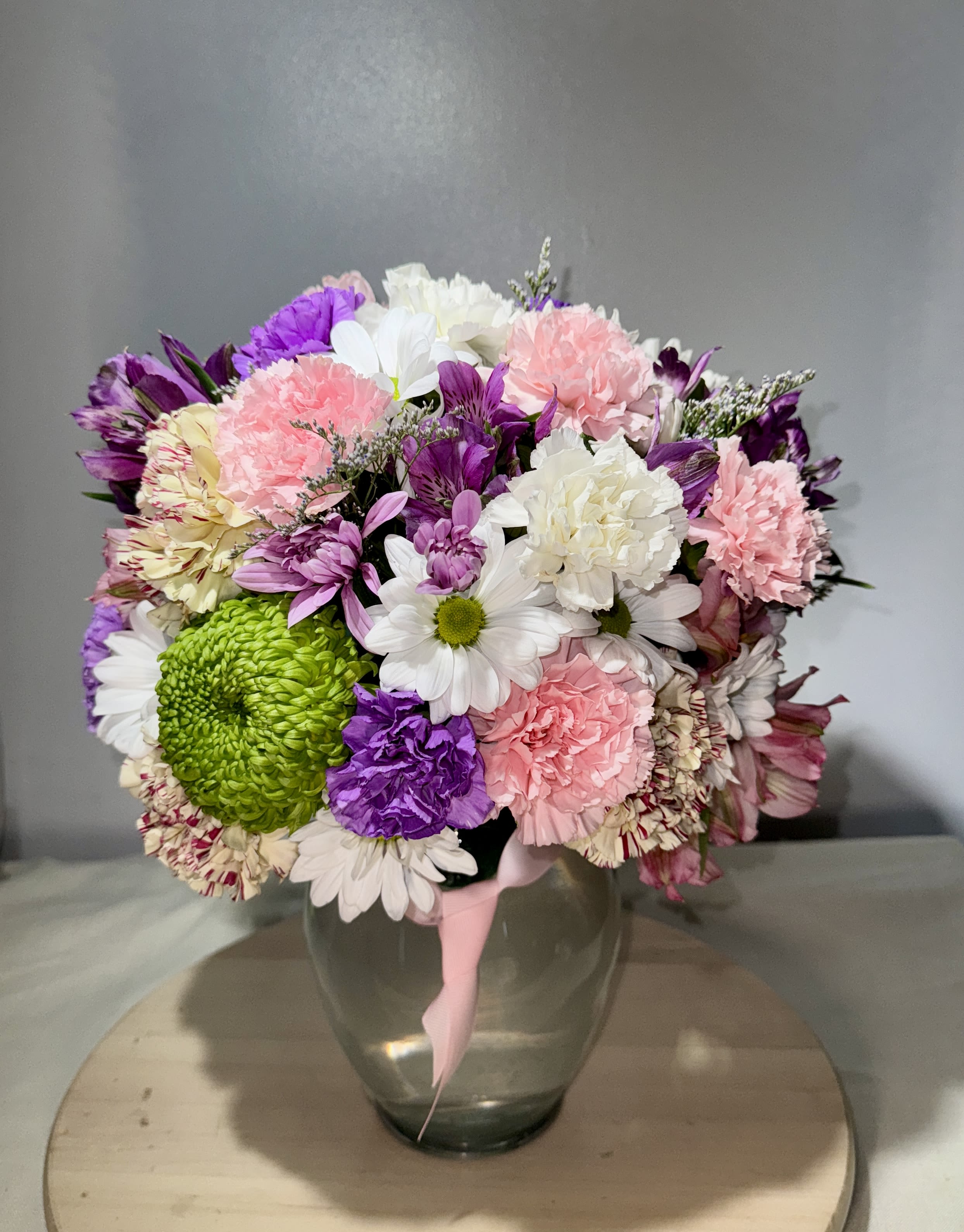 Mixed bouquet of pink, purple, white, and green flowers in a glass vase