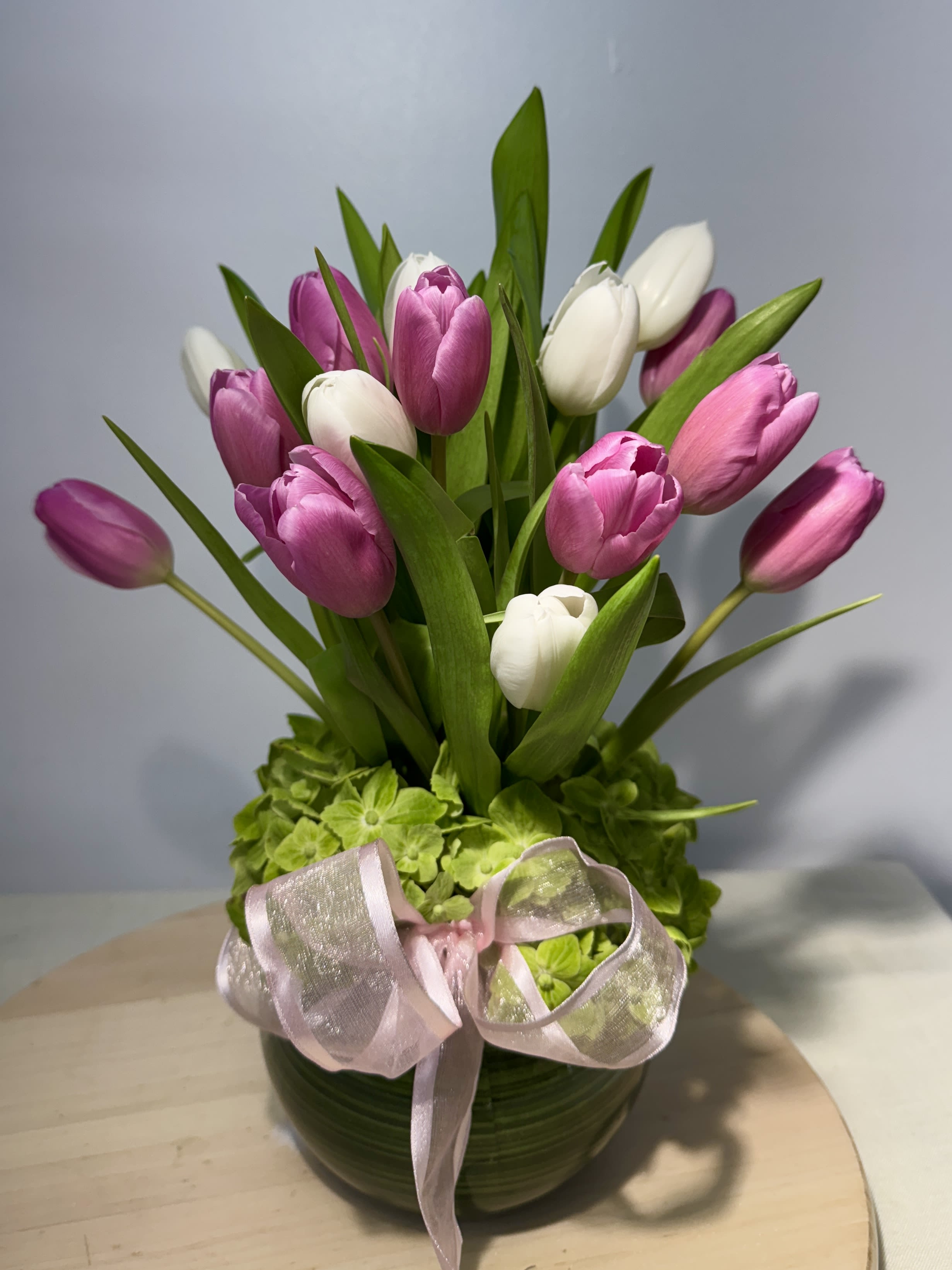 Pink and white tulips arranged in a round vase with a ribbon bow